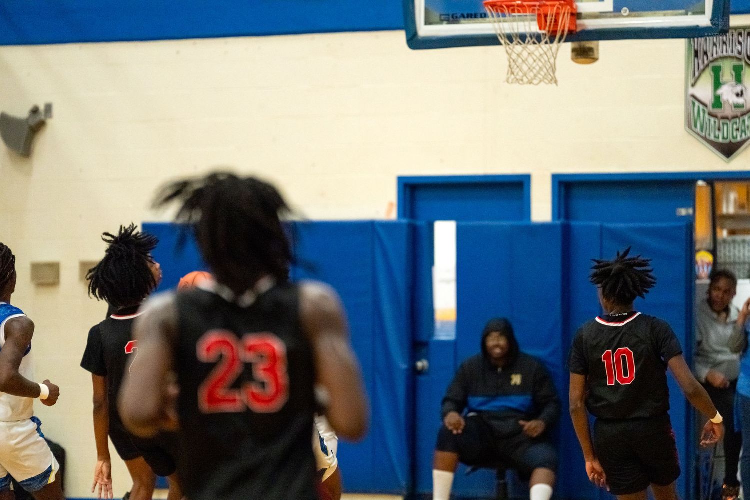 Opposing team players #23 and #10 in black uniforms stand near the basket during a basketball game.