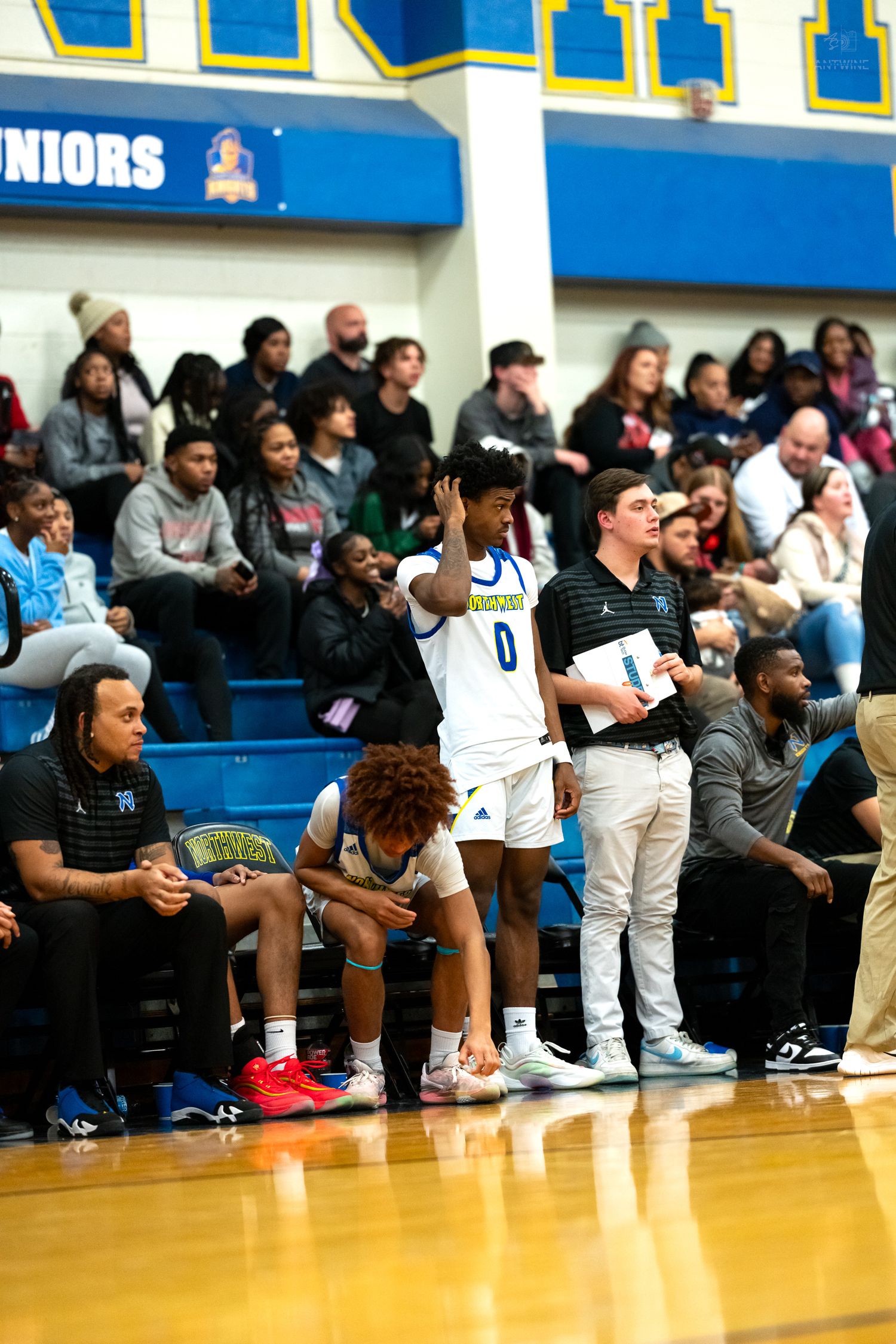 Northwest basketball player #0 signals from the sideline bench during a high school game.