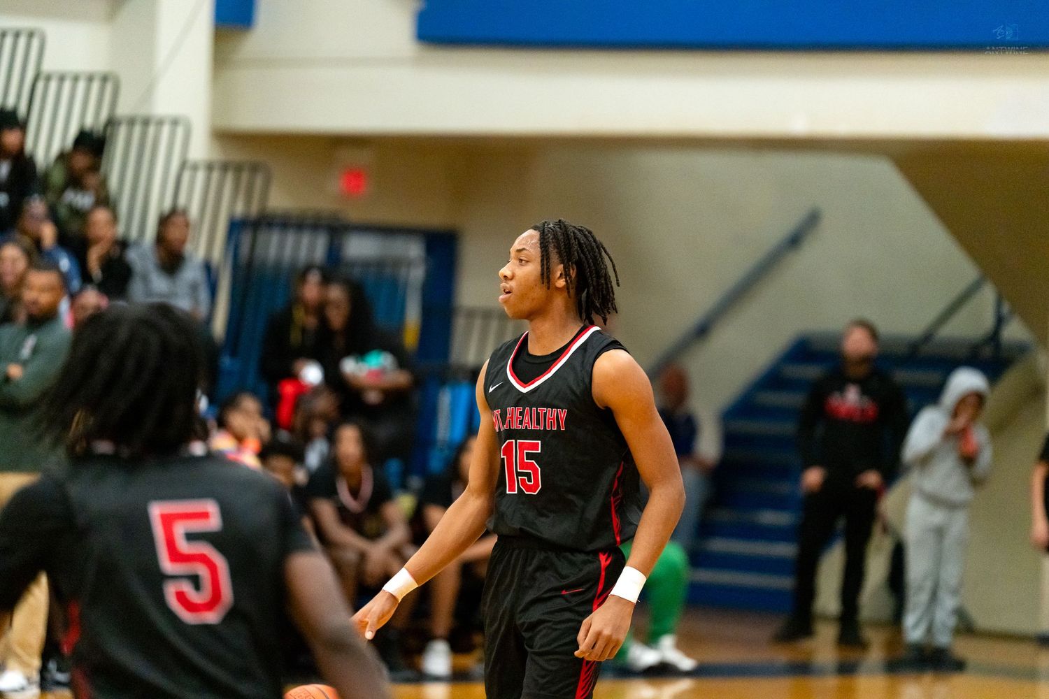 Player number 15 in a black jersey stands on the court during a high school basketball game.