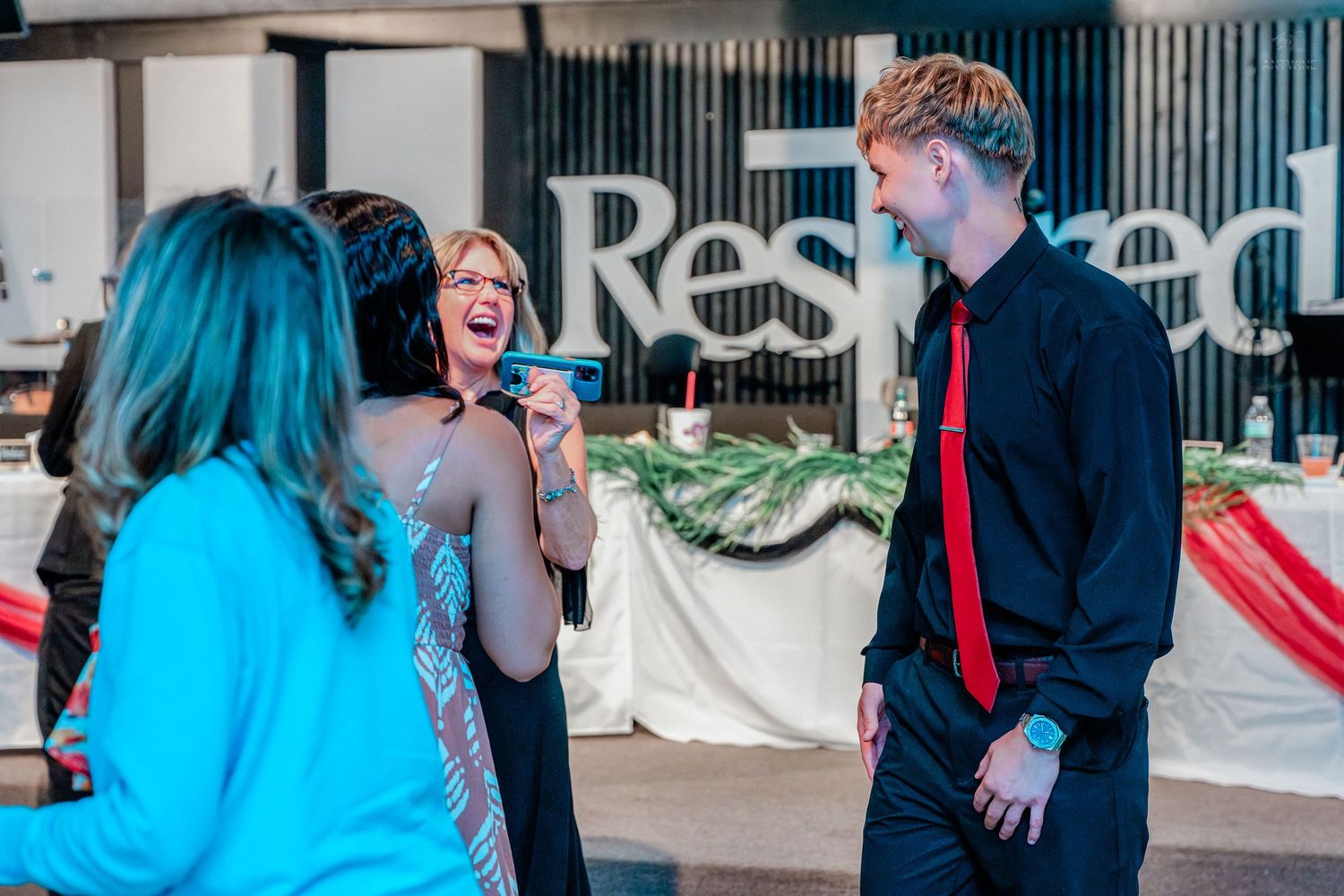Group of people laughing and socializing at a formal event in front of a decorated backdrop.