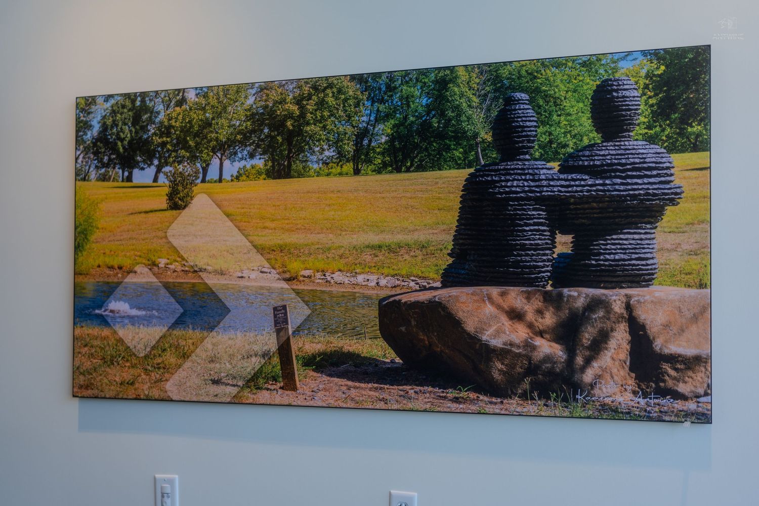 Large canvas wall art print of two tire sculptures sitting on a rock overlooking a sunny green park landscape.