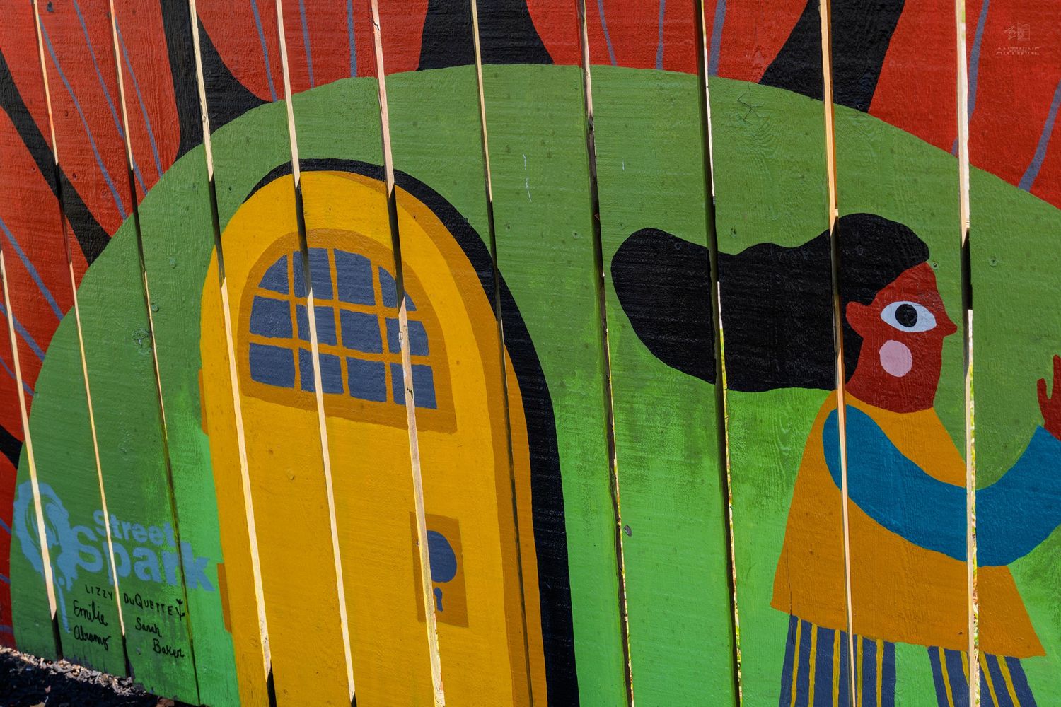 Colorful street mural on wooden fence featuring a yellow door, green arch, and abstract figure with red and blue accents.