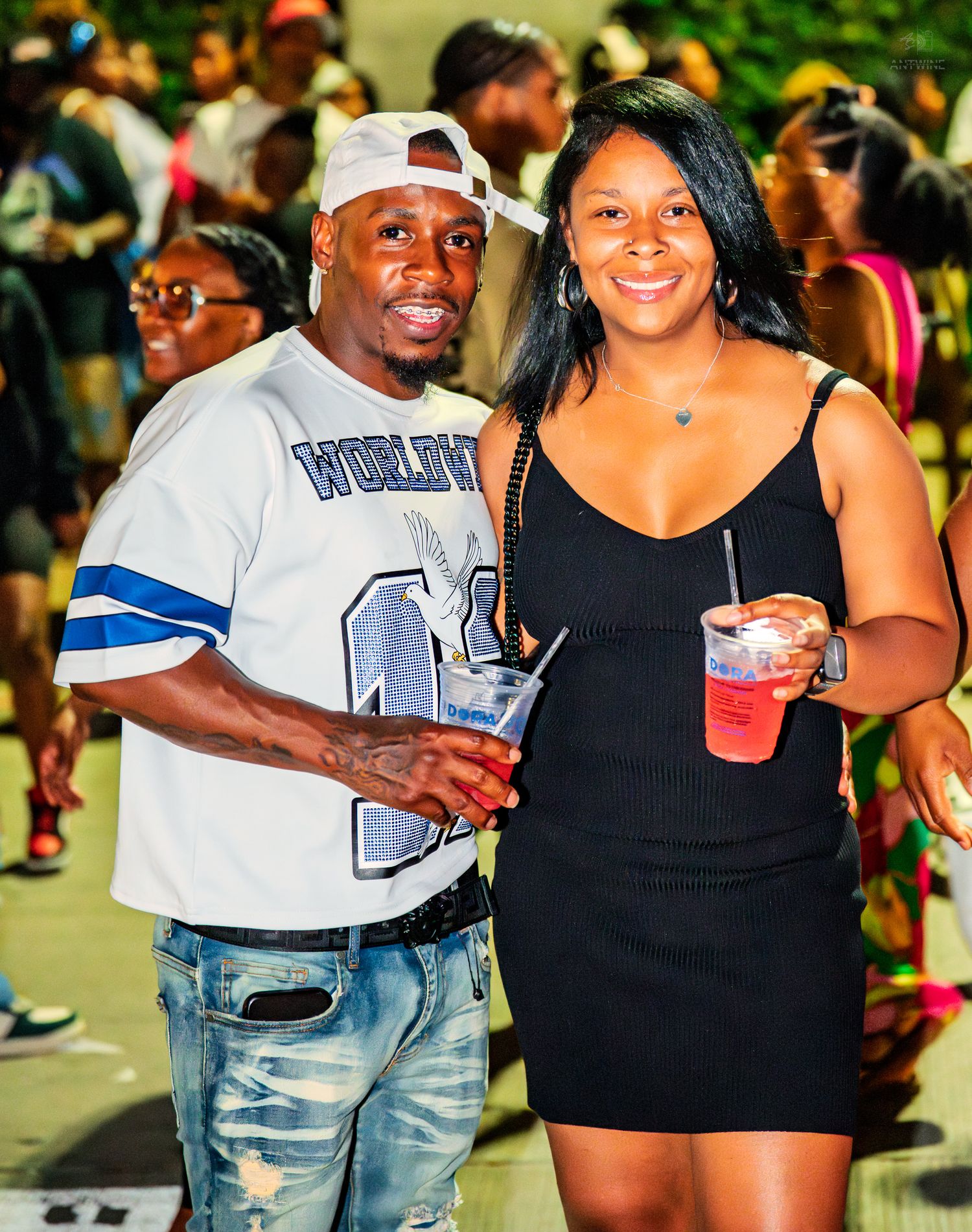 Two friends smile and hold colorful drinks at an outdoor night party event.