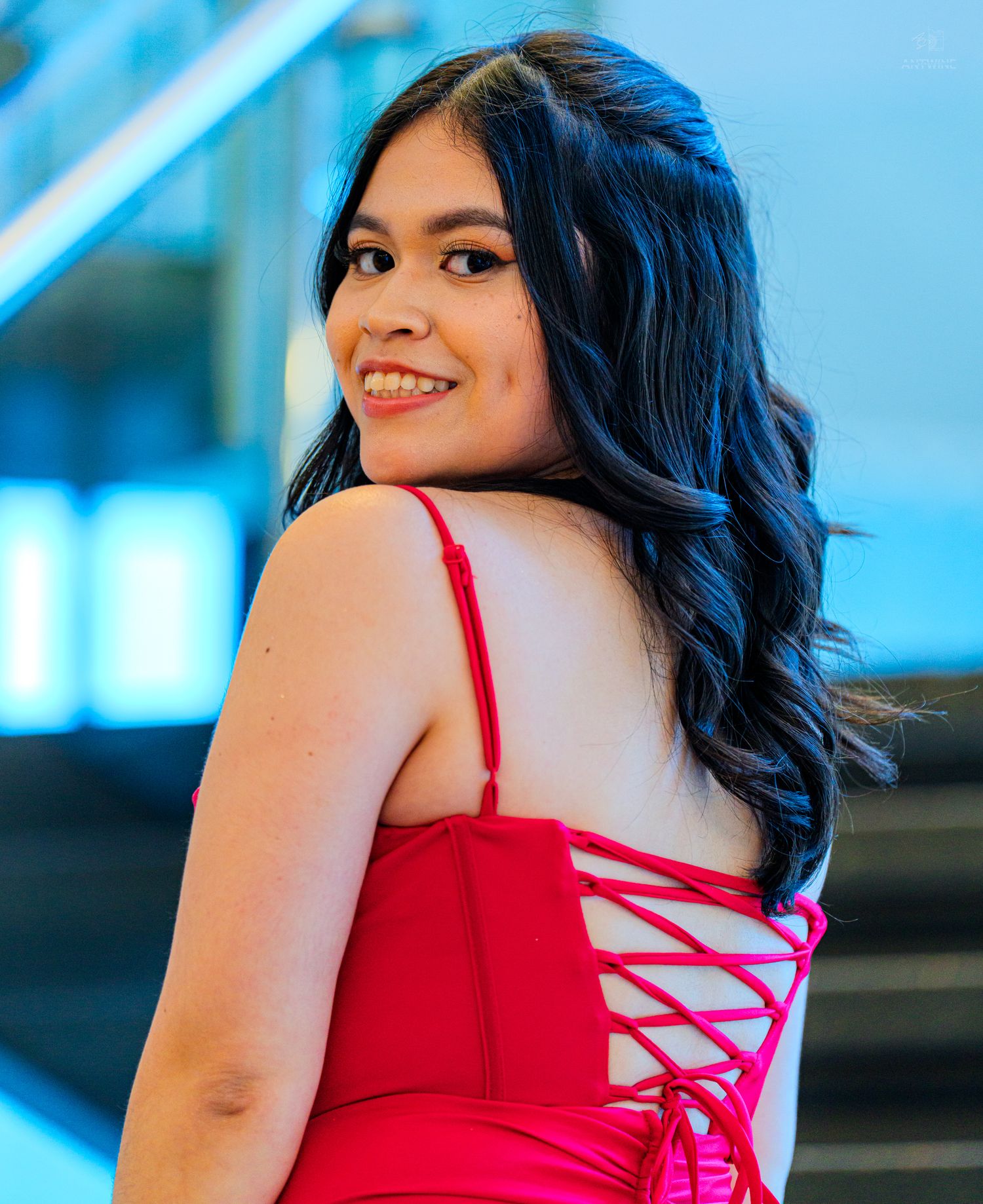 Young woman in red lace-back dress smiling over shoulder on modern staircase.