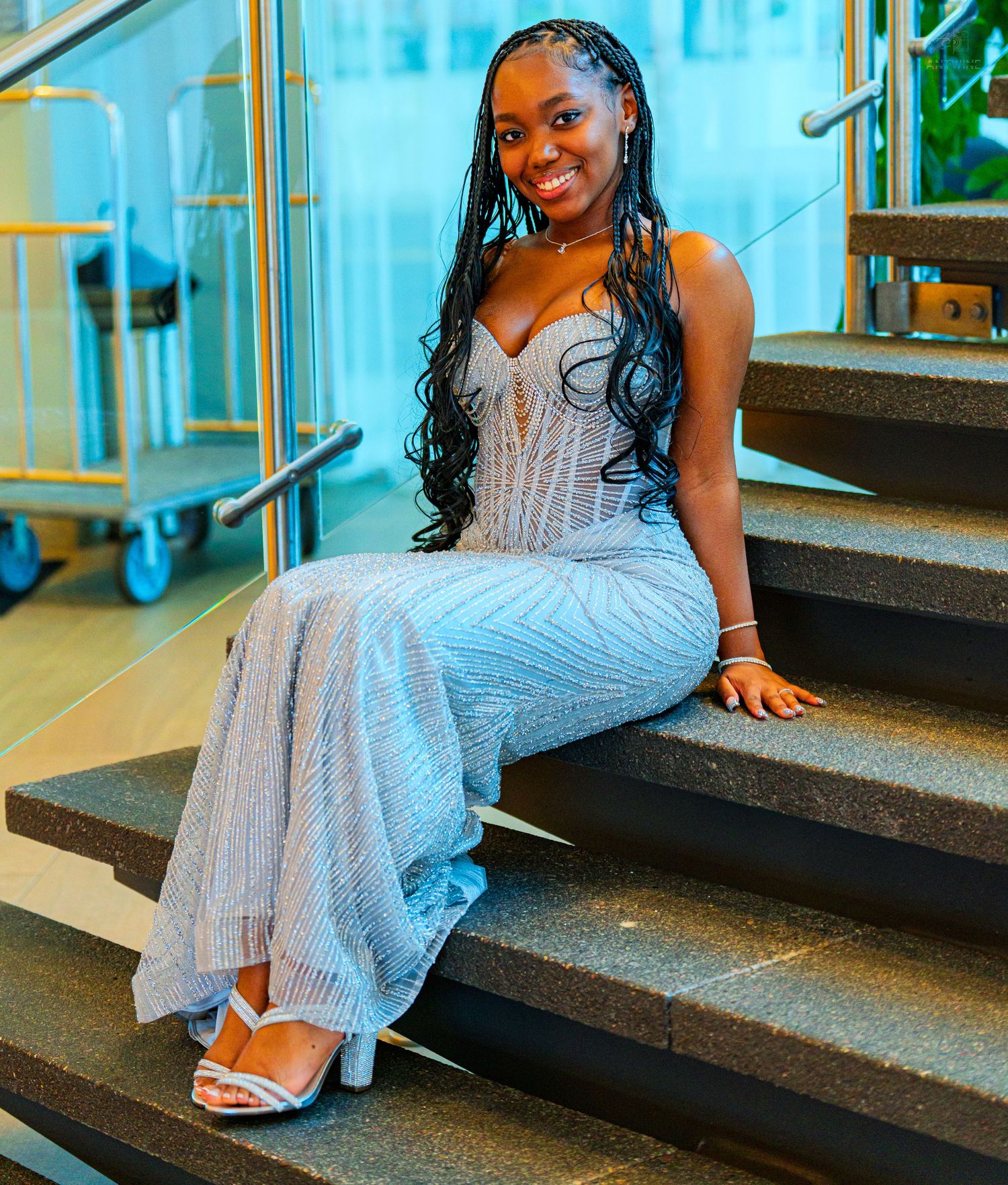 Young woman in silver sequin gown sitting on stairs, wearing white heels and long braids.