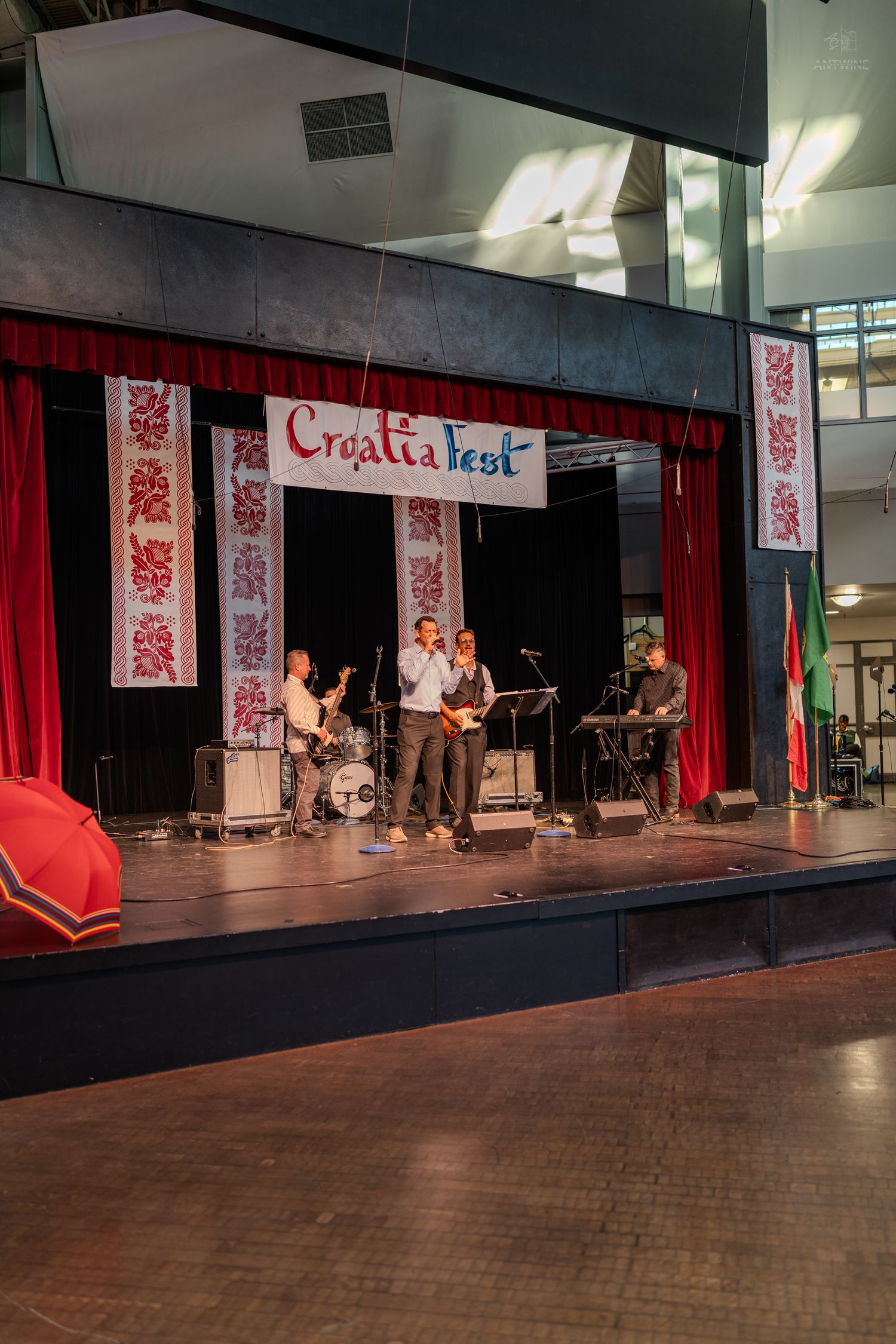 Band performing on stage at Croatia Fest with red curtains and traditional embroidered decorations.