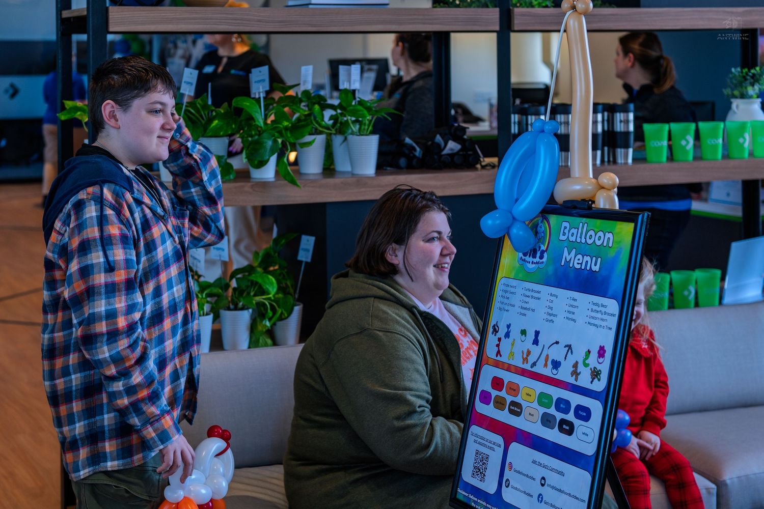 Two people stand near a colorful Balloon Menu display inside a modern venue with plants and shelves.
