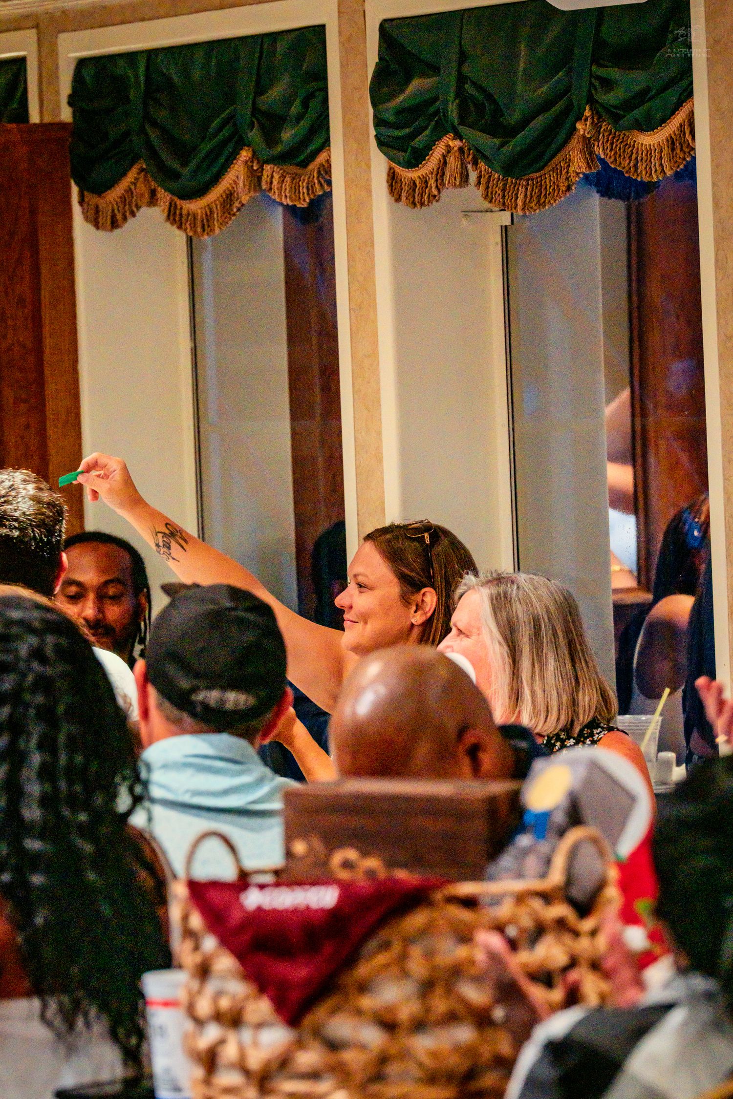 Diverse group of guests socializing at an elegant indoor banquet event with green drapes.