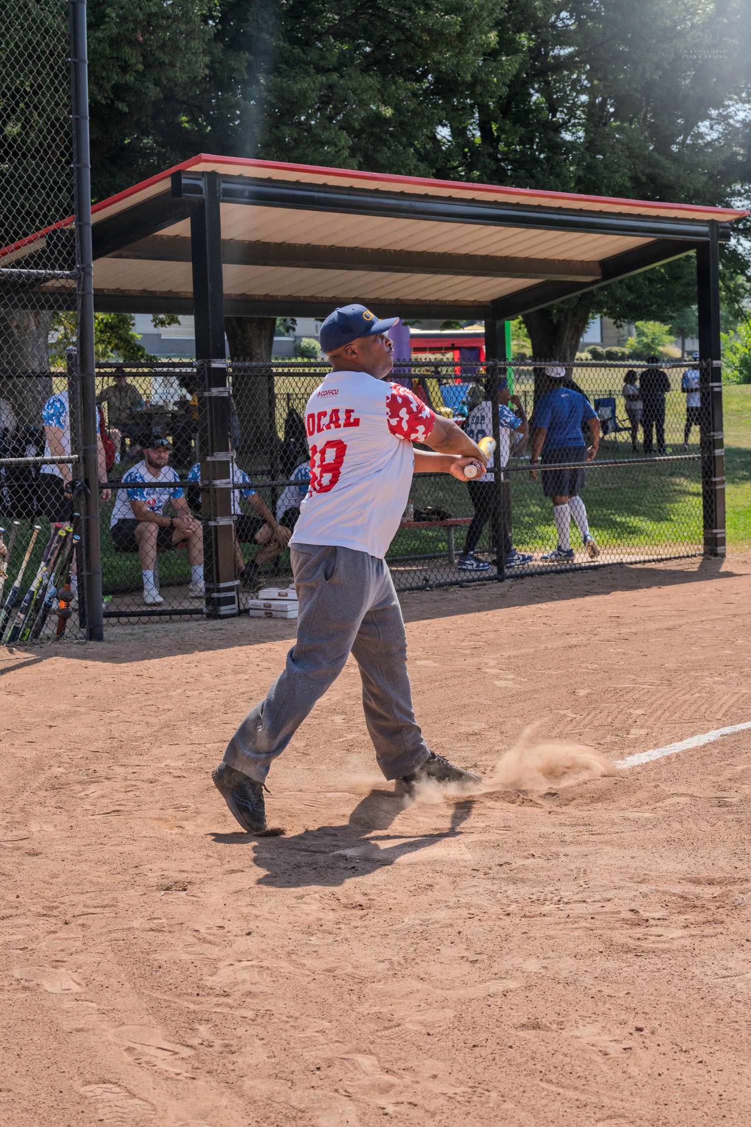 Youth baseball player swinging bat at home plate during a little league game on a dirt field.