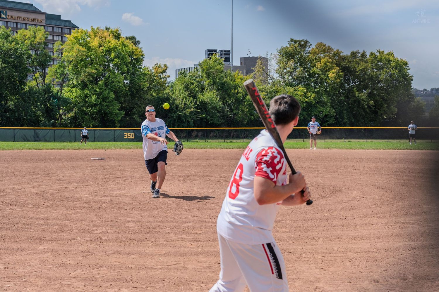Softball pitcher throwing to a batter during an outdoor recreational game on a sunny summer day.