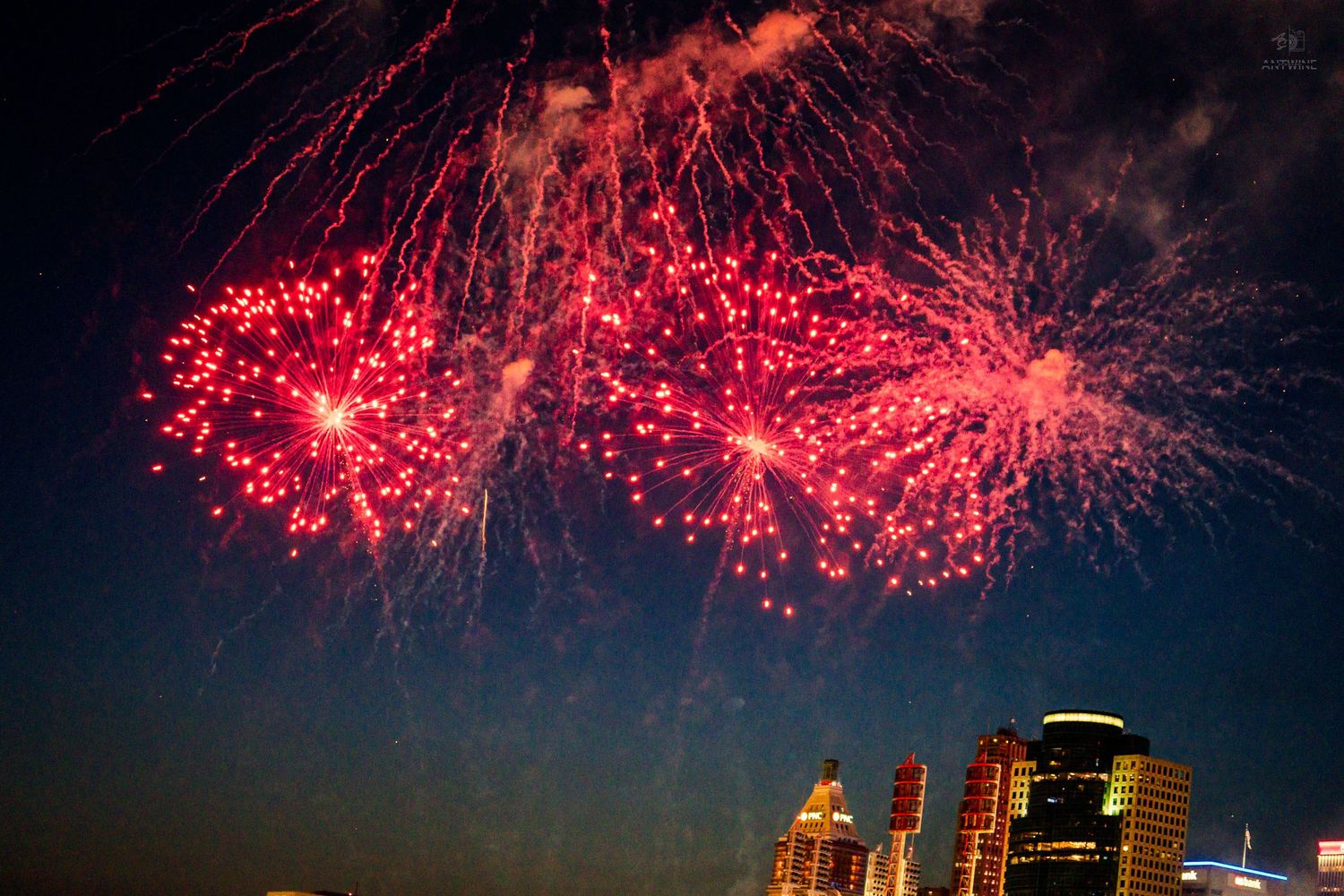 Red fireworks exploding over a city skyline at night with glowing buildings below.