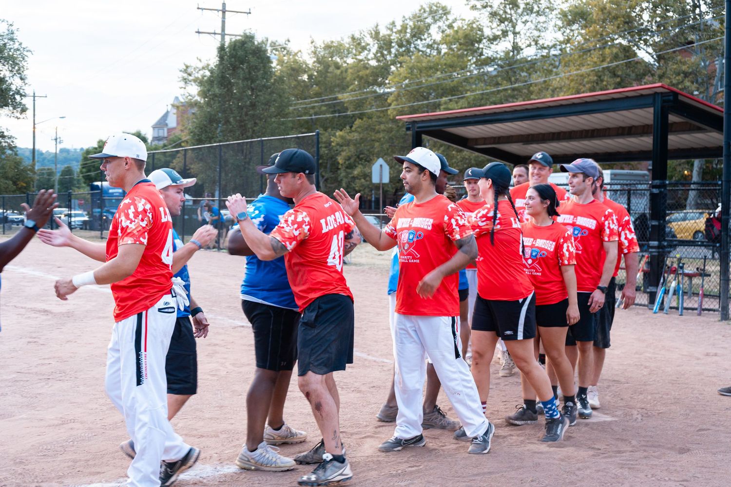 Teams in red and white uniforms exchange high-fives on a baseball field after a friendly game.