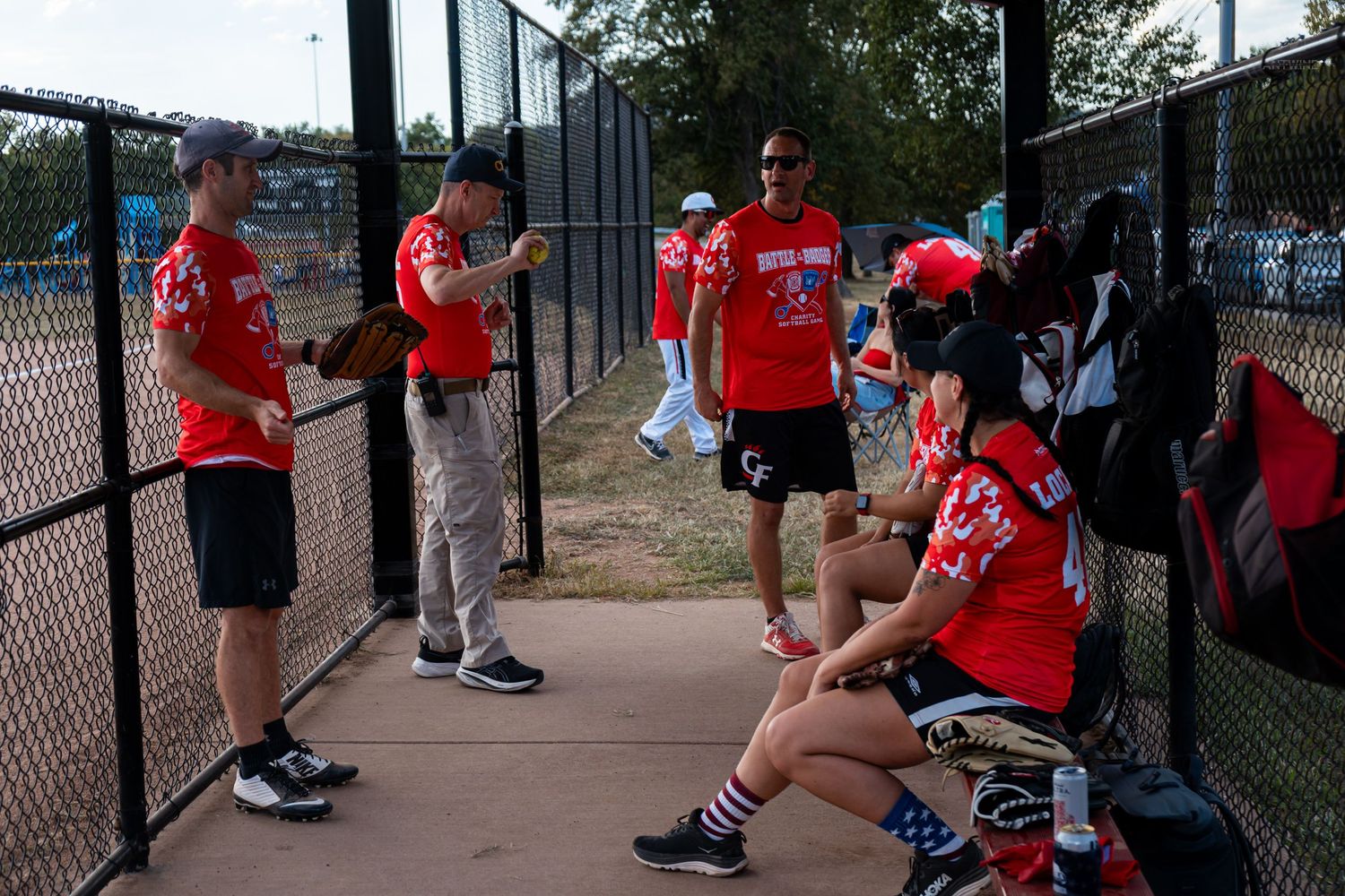 Softball players in red uniforms gather in the dugout discussing strategy before their game.