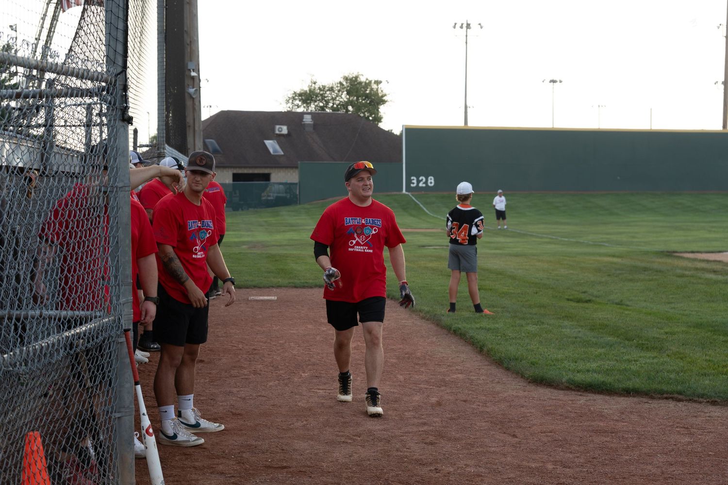 Baseball players in red uniforms walking along the dirt path beside a chain-link fence on an outdoor baseball field.