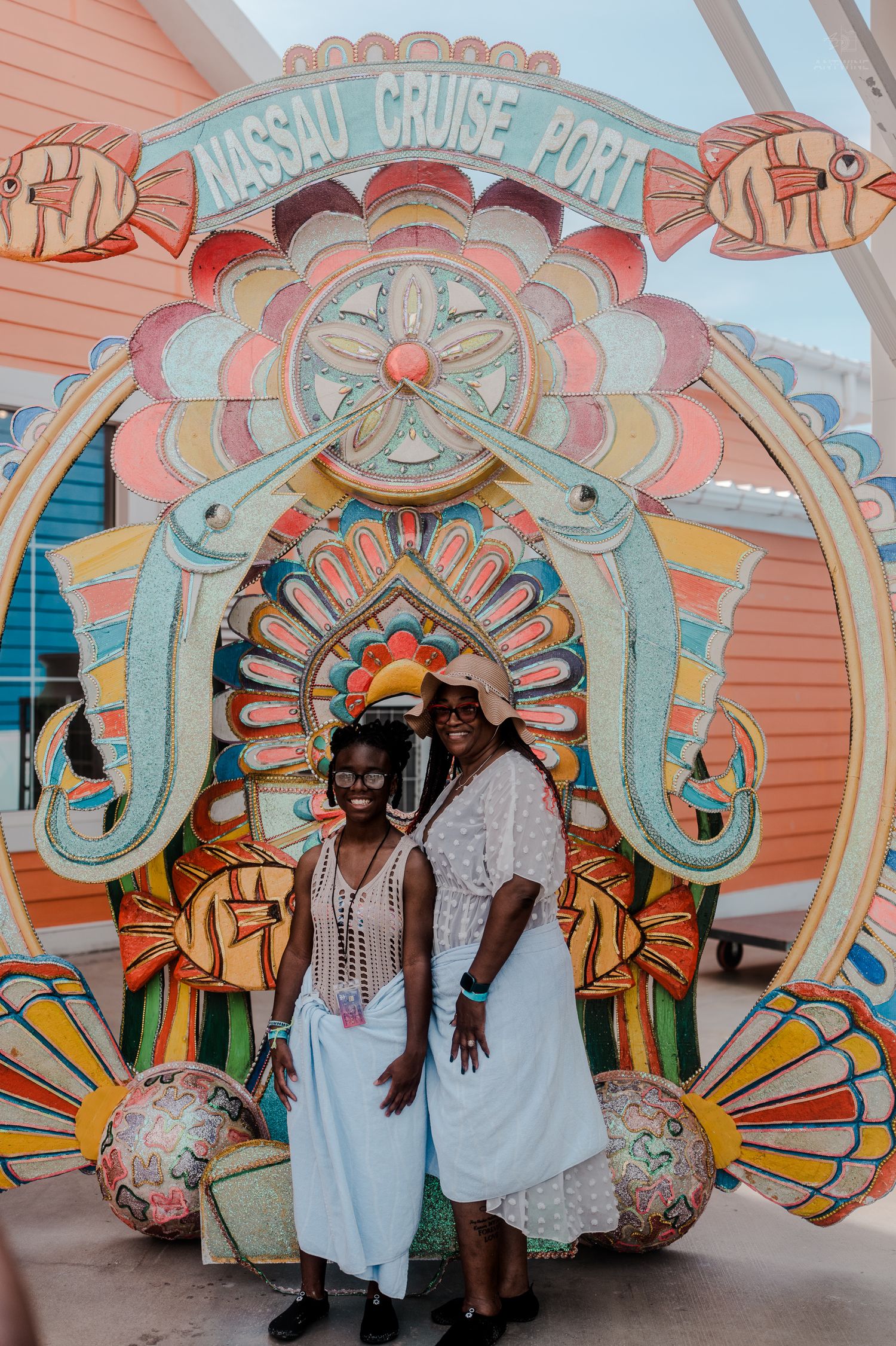 Two women in white outfits pose in front of the colorful Nassau Cruise Port decorative entrance sign.