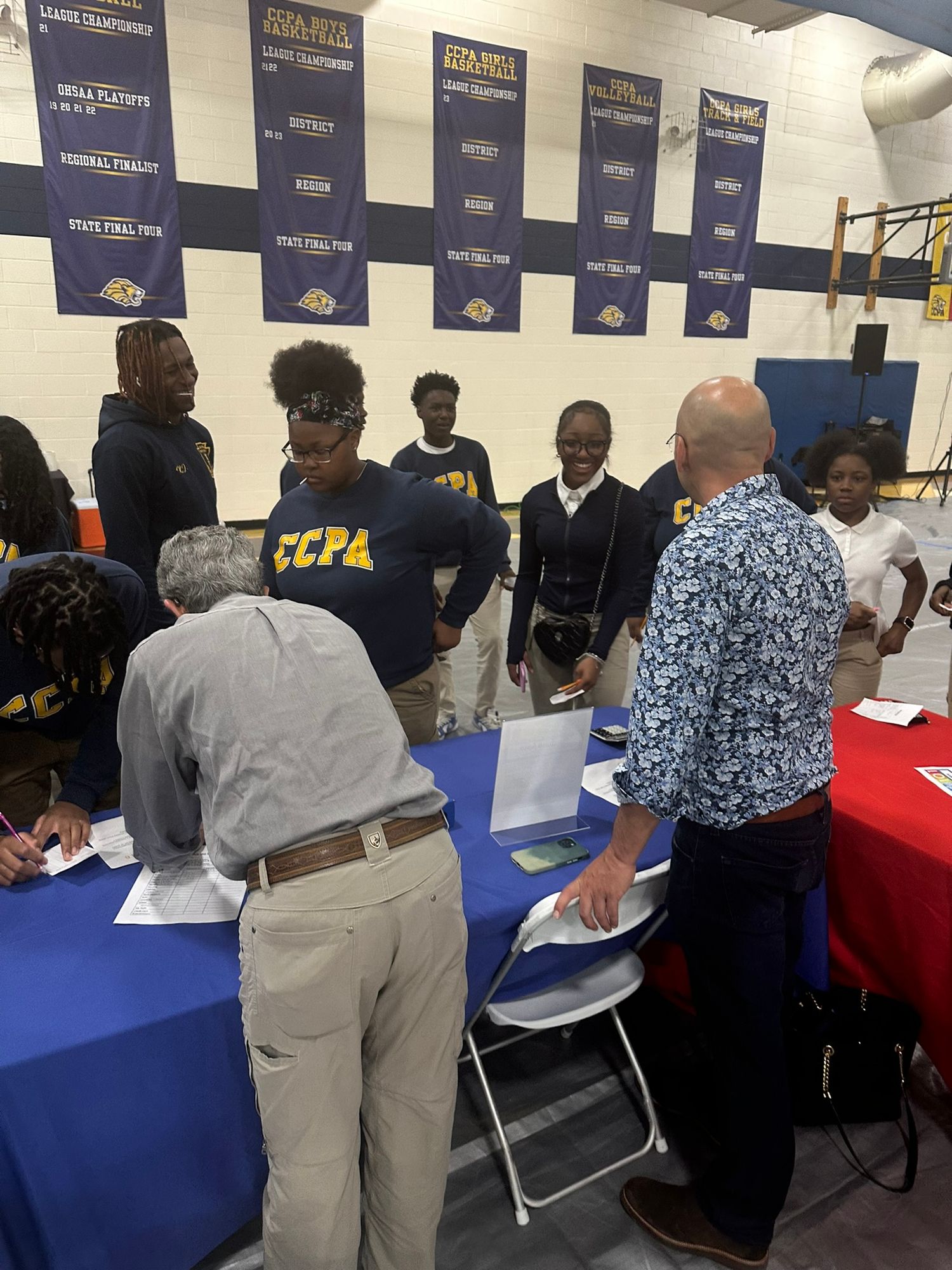 Students in CCPA uniforms gather at tables during a school signing or registration event in a gymnasium.