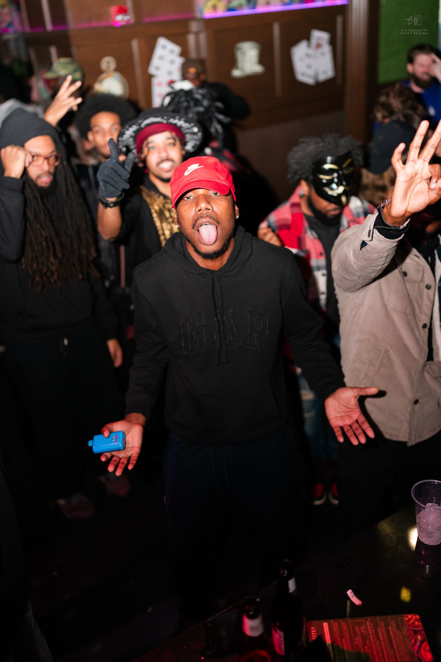 Energetic man in red cap posing with crowd at a lively bar party.