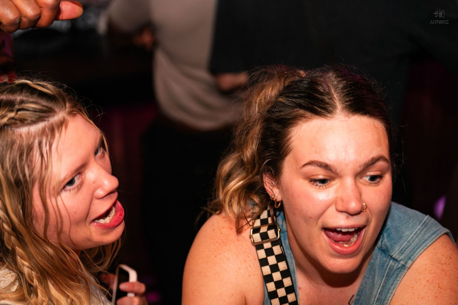 Two women making silly faces and sticking out tongues at a nightclub party.