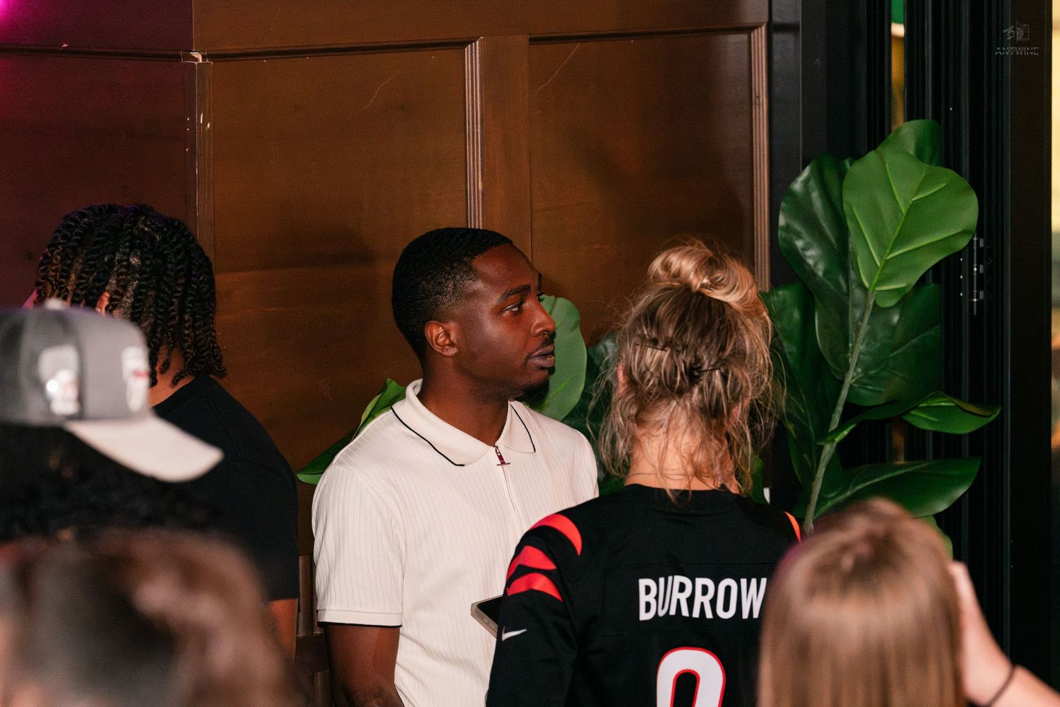 Young man in white polo shirt socializes at a crowded nightclub event.