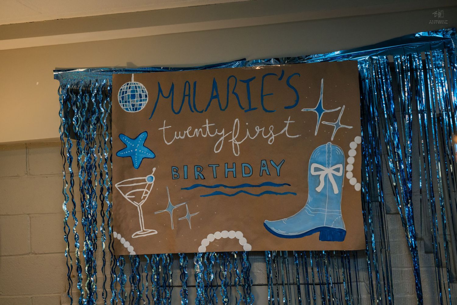 Handmade sign reading Malarie's Twenty First Birthday decorated with blue cowboy boot and tinsel.