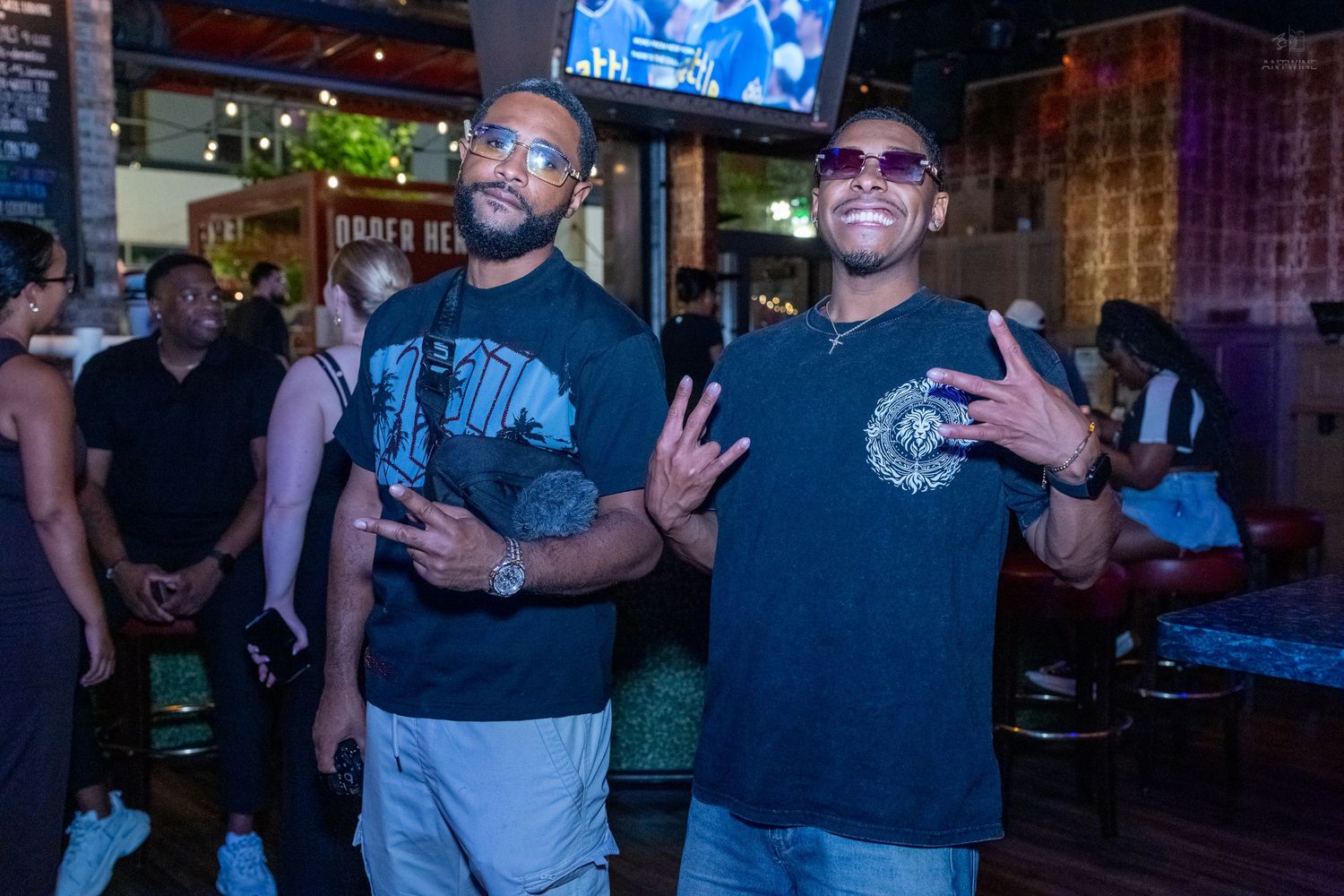 Two men throwing hand signs and posing together inside Stretch Bar lounge.