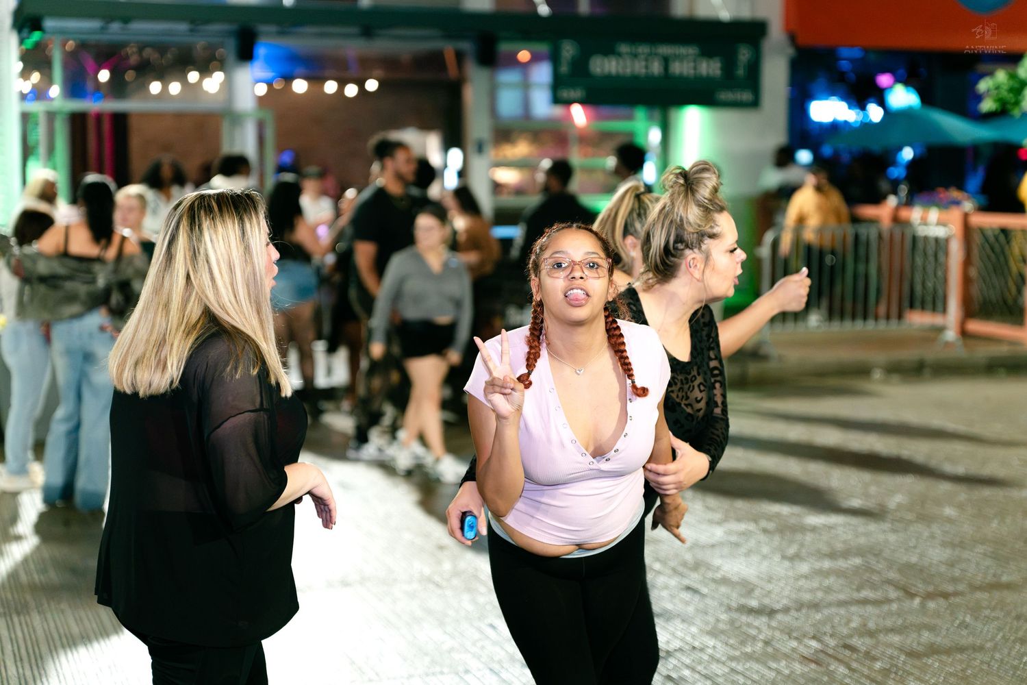 Women socializing on busy outdoor street at night near illuminated venue signage.