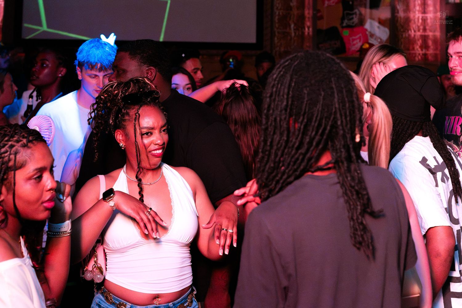 Young woman smiling and dancing in white crop top at a lively nightclub party.