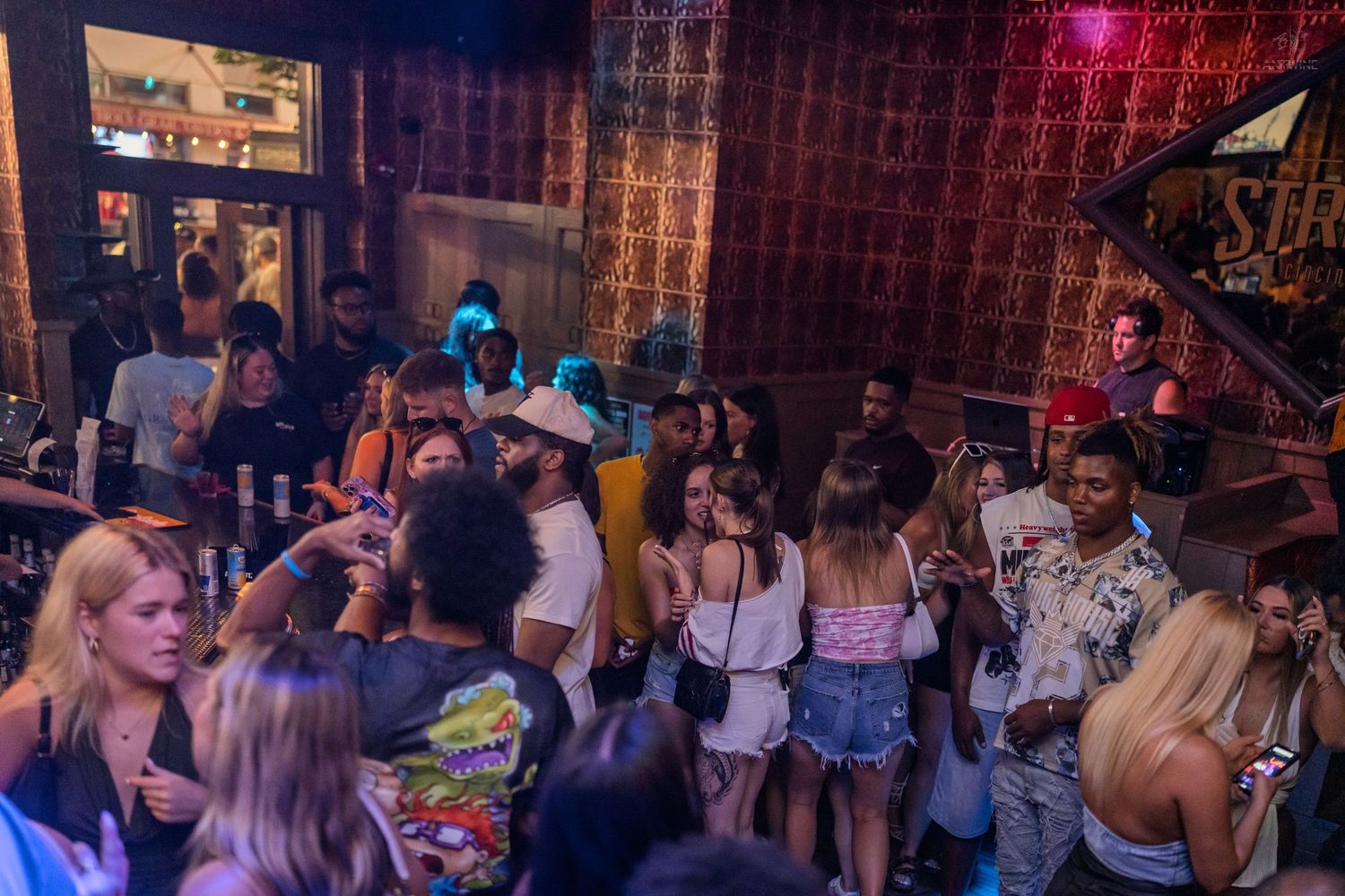 Diverse group of partygoers mingling in a dimly lit bar with warm ambient lighting.