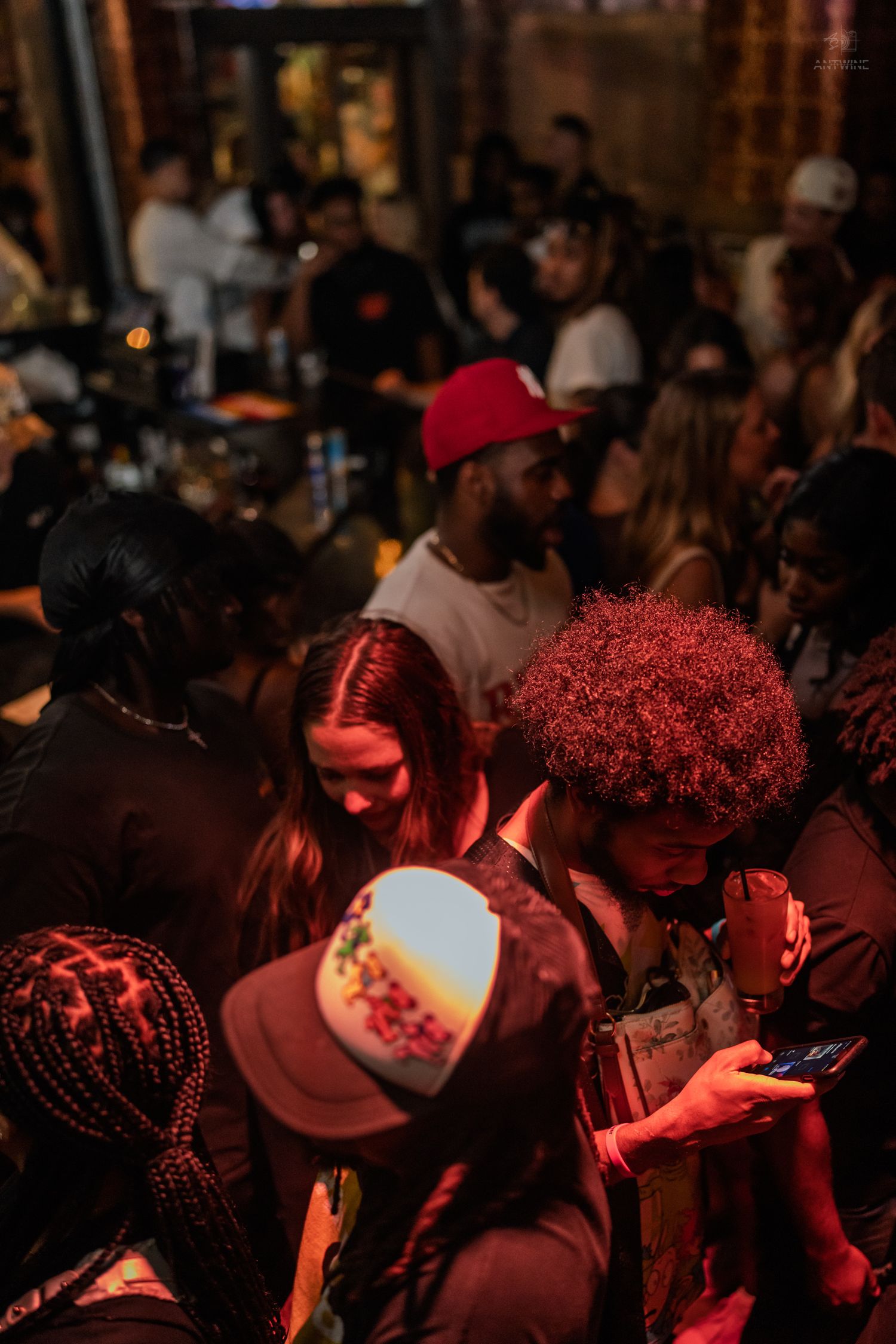 Diverse crowd gathered at a nightclub under warm red lighting during a busy event.