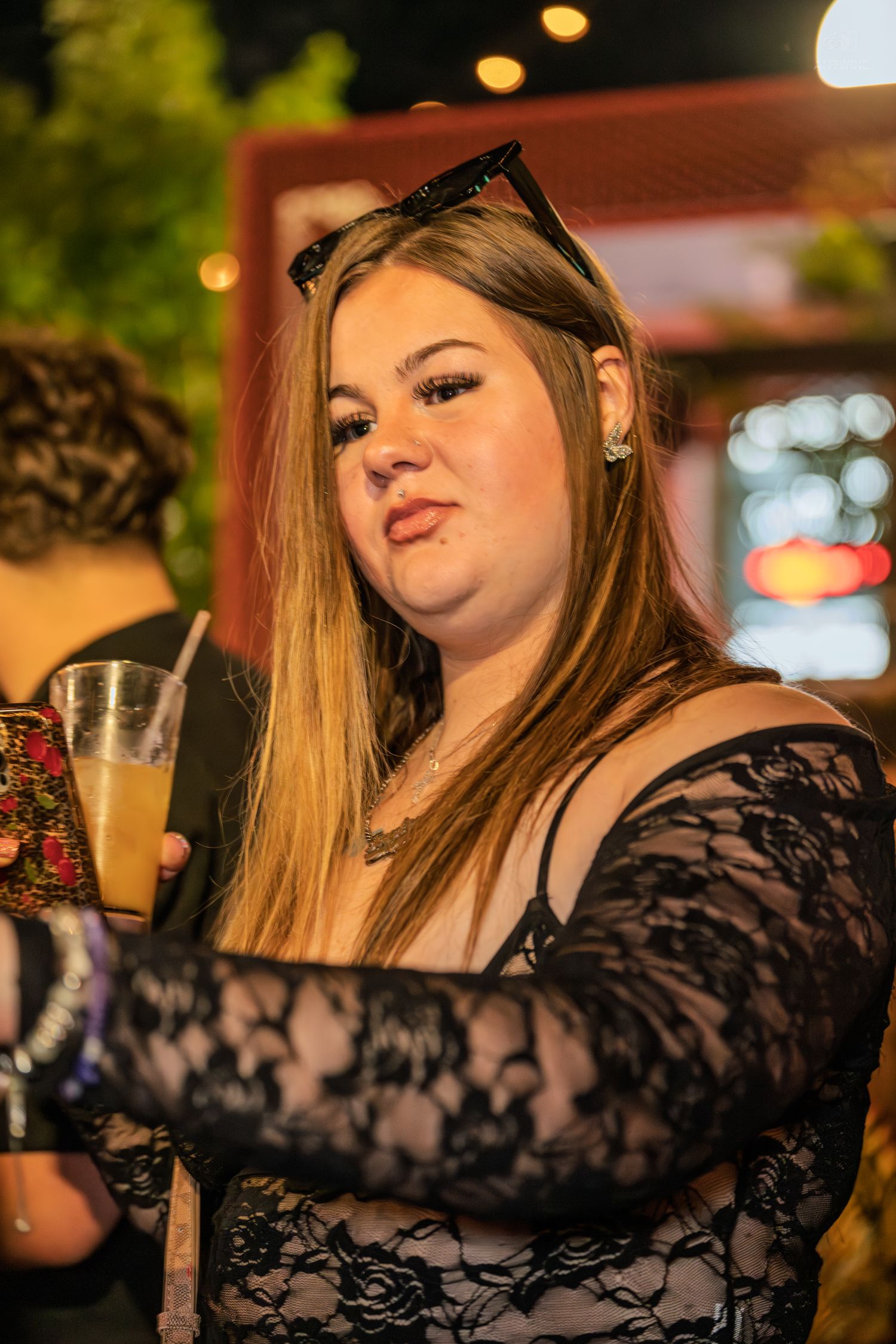 Young woman in black lace top holding a drink at an outdoor evening party.