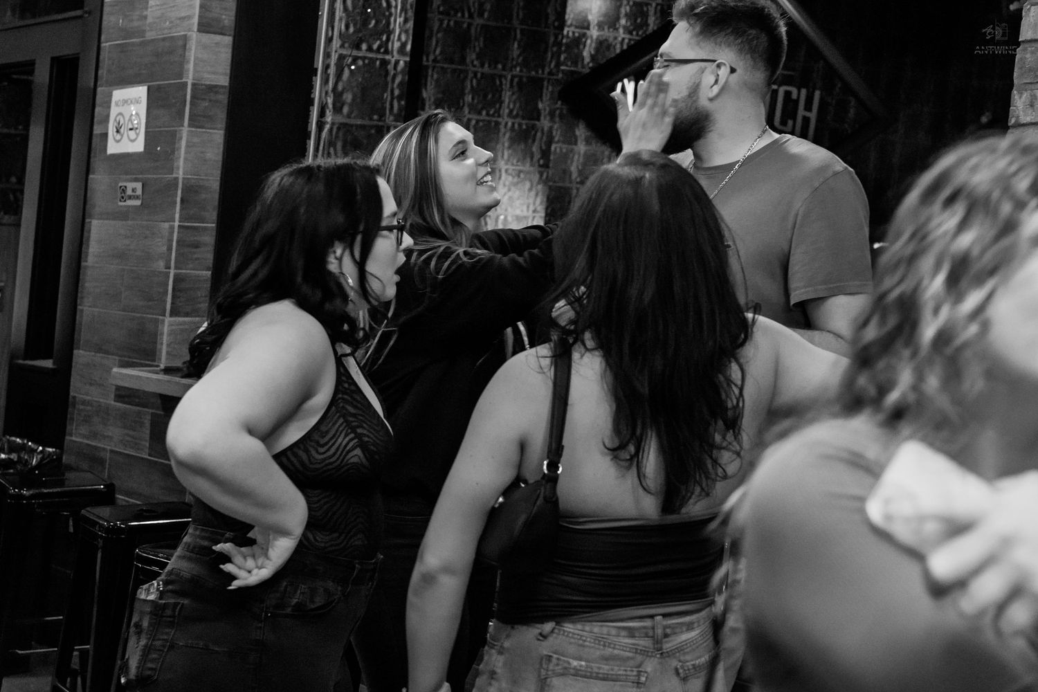 Black and white candid photo of a group of friends talking and laughing outside a bar entrance.