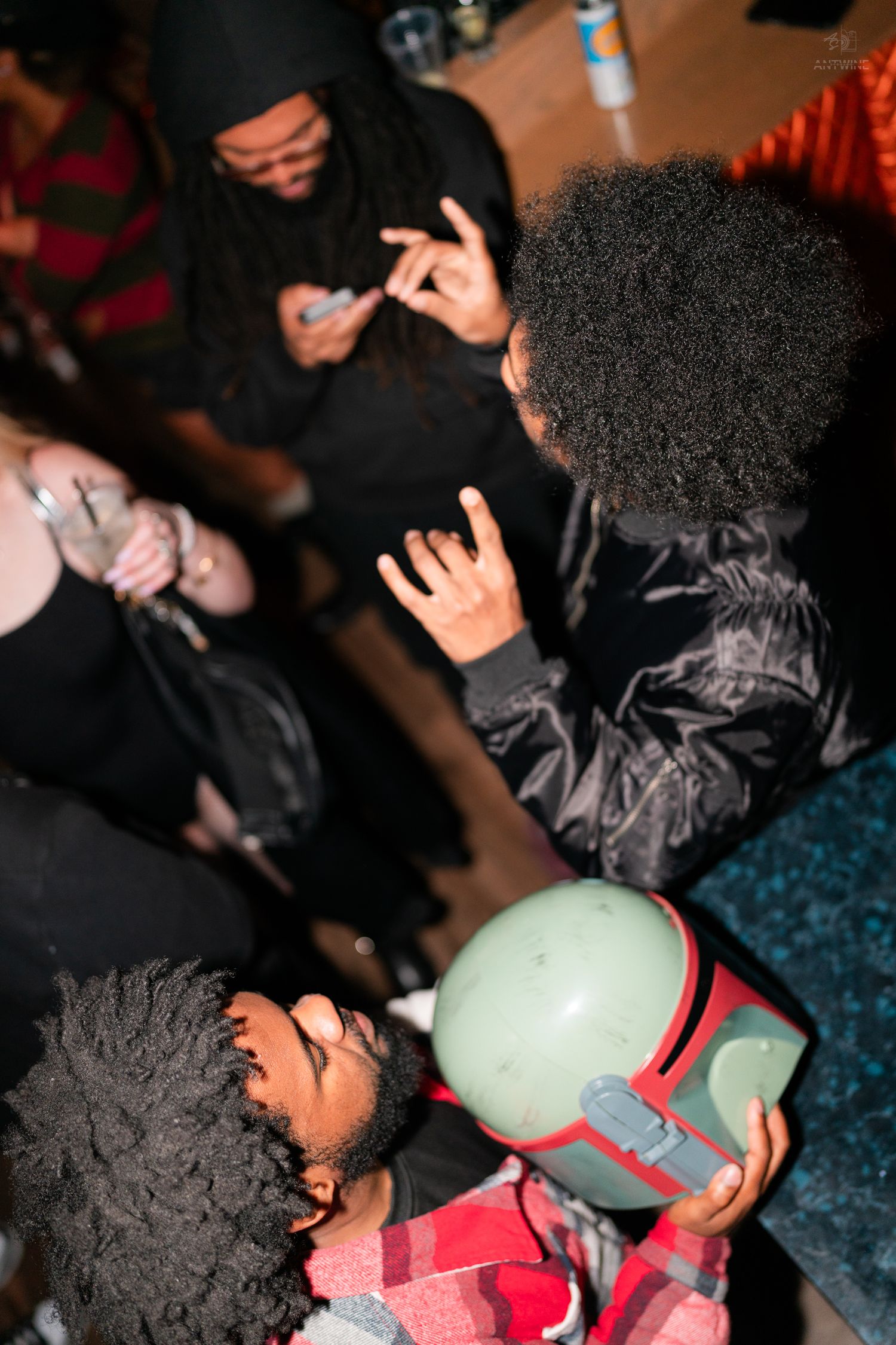 Group of people at Halloween party with Boba Fett helmet visible in foreground crowd.