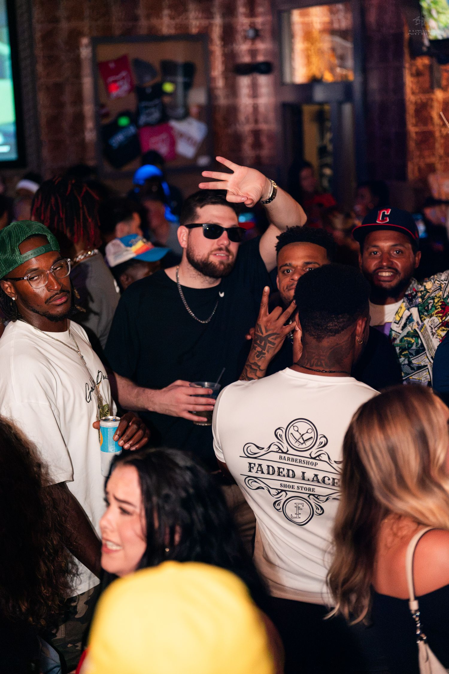 Man in sunglasses waving at a lively indoor nightclub gathering.