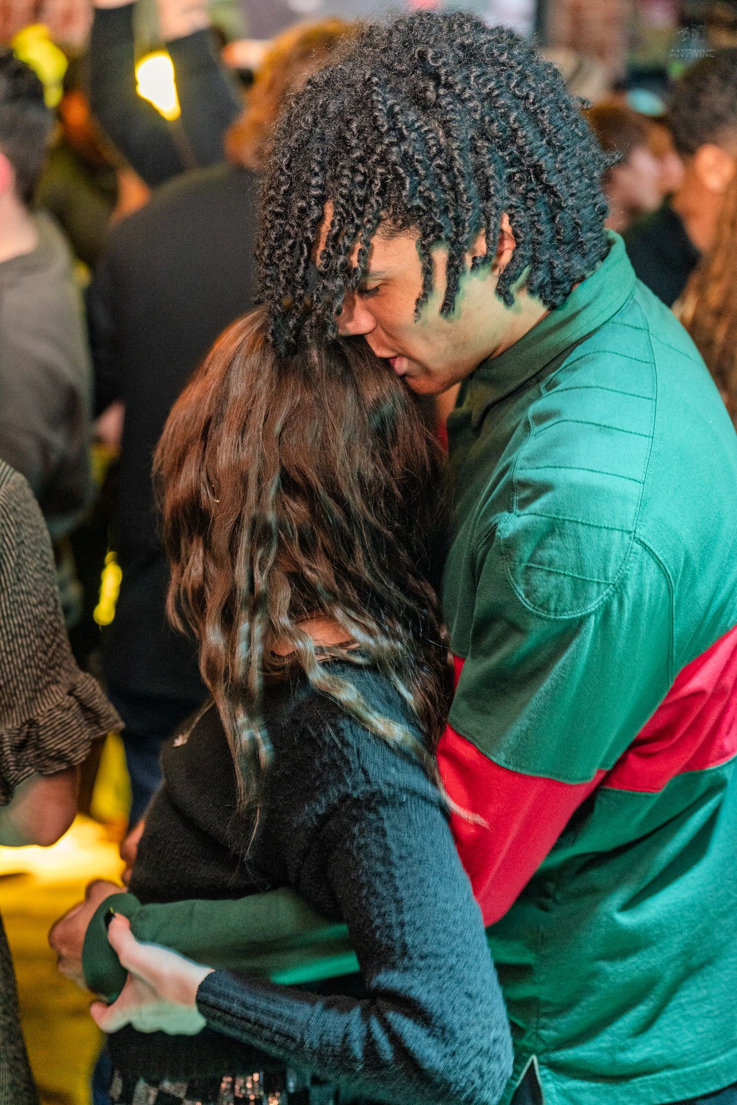 Couple embracing closely at a vibrant social gathering with colorful lighting.