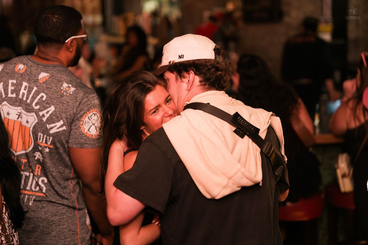 Couple embracing warmly in a crowded outdoor bar or street event at night with people in the background.