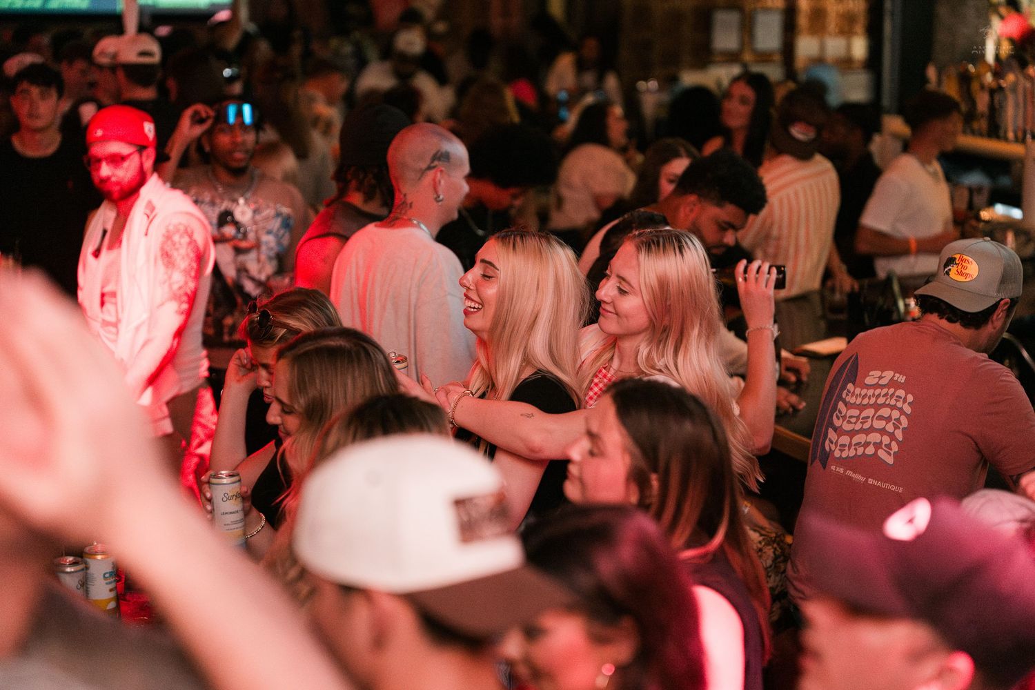 Crowd of people socializing and dancing at a lively bar nightlife event with red ambient lighting.