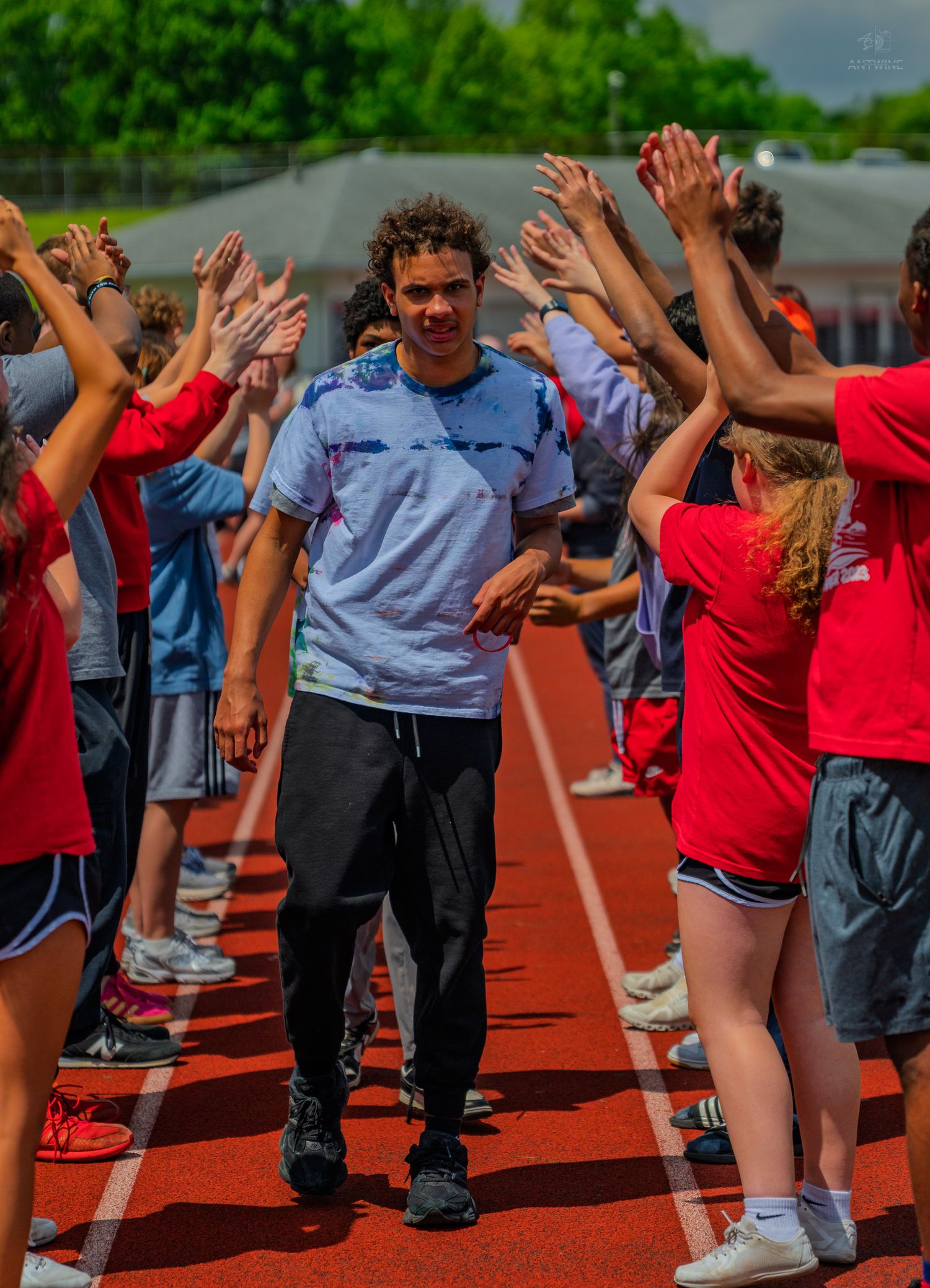 Young athlete walks through a celebratory high-five tunnel on a red track surrounded by cheering peers outdoors.