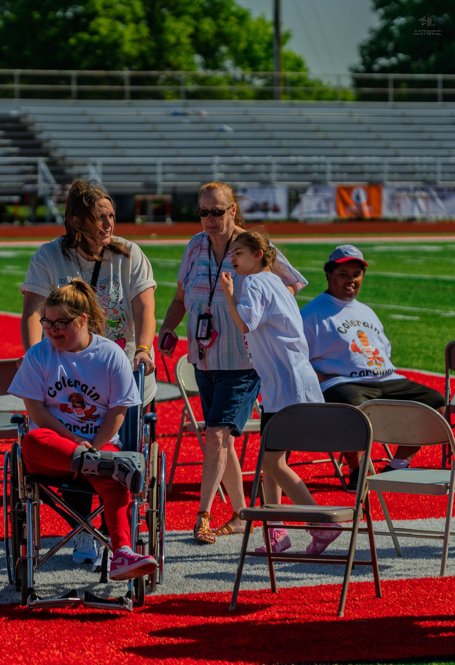 People at an outdoor stadium event, including wheelchair users in matching shirts, gathered on a red track field.