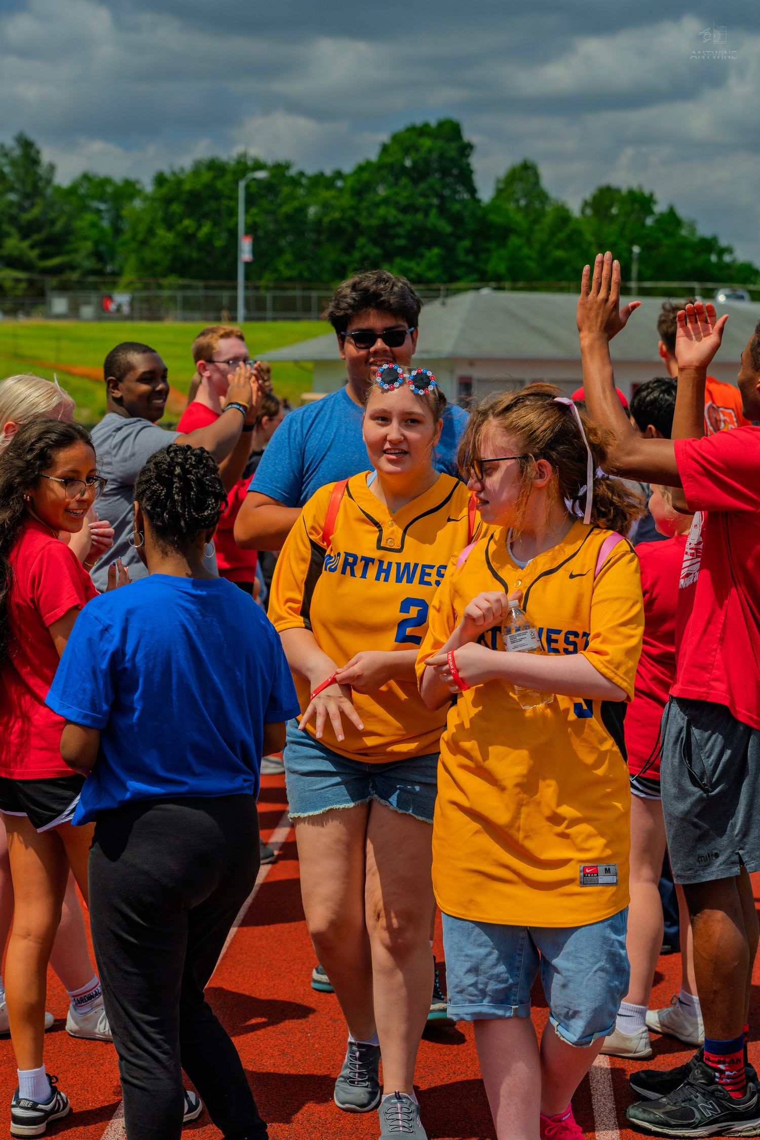 Two girls in Northwest jerseys walk through a congratulatory high-five line at an outdoor track event.