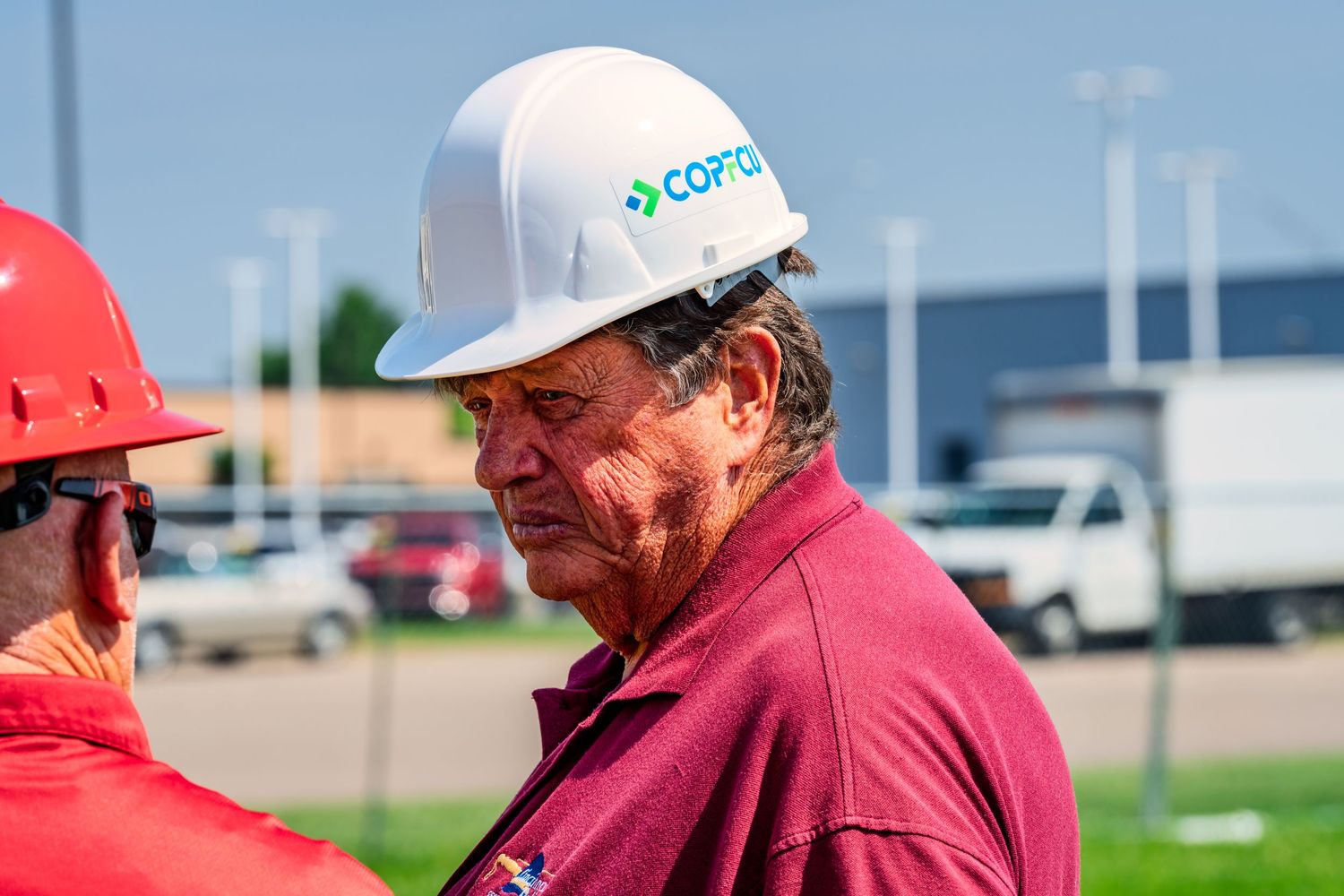 Man in COPFCU white hard hat at an outdoor construction site on a sunny day.
