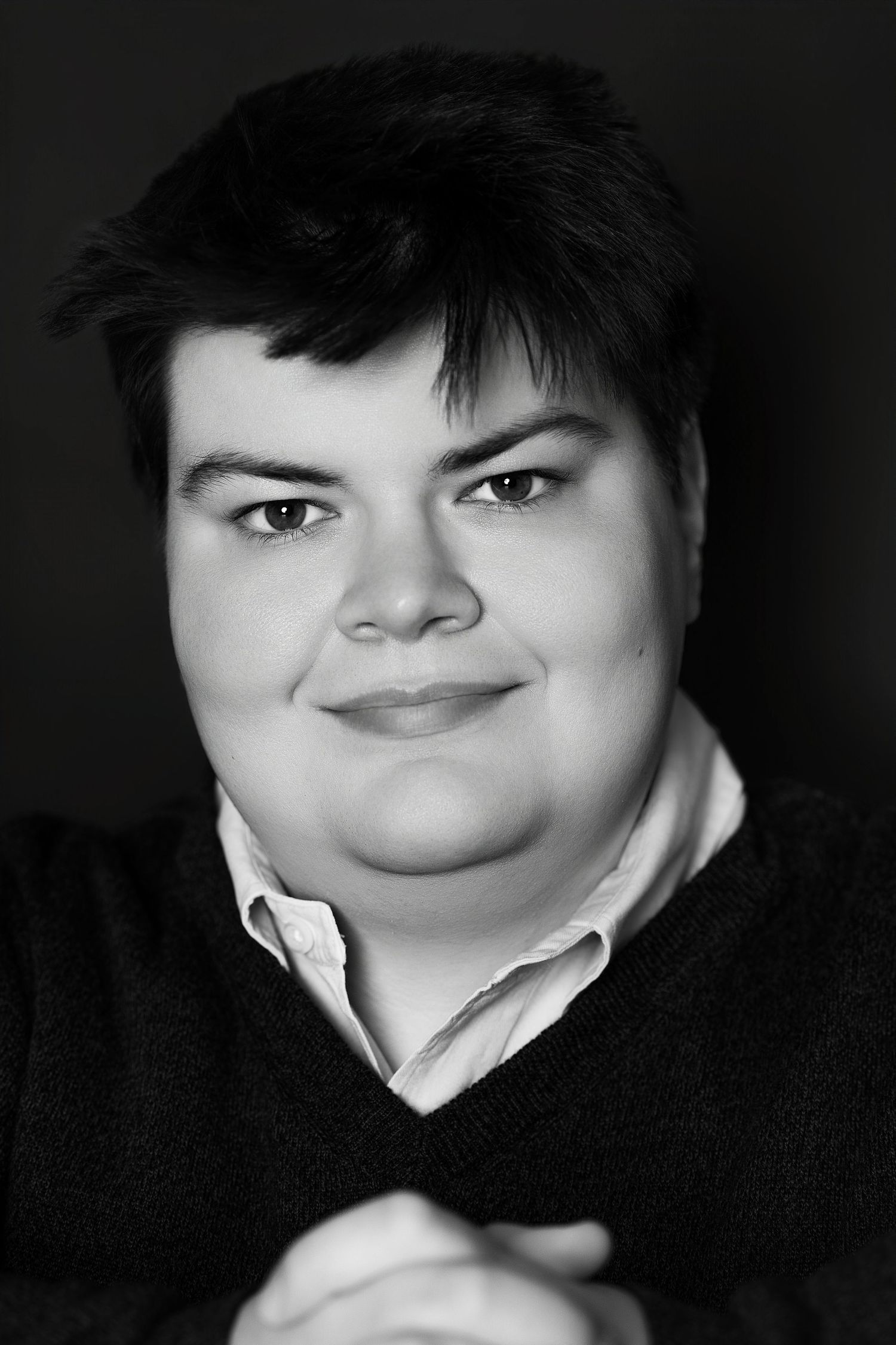 Black and white close-up portrait of a young person with short dark hair smiling softly.