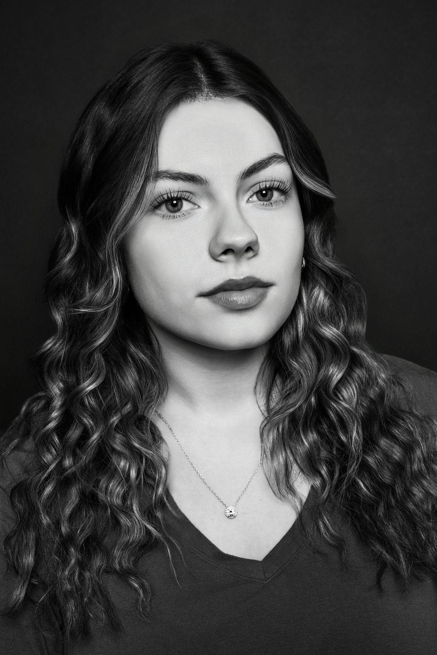 Elegant black and white close-up portrait of a young woman with long curly hair and necklace.