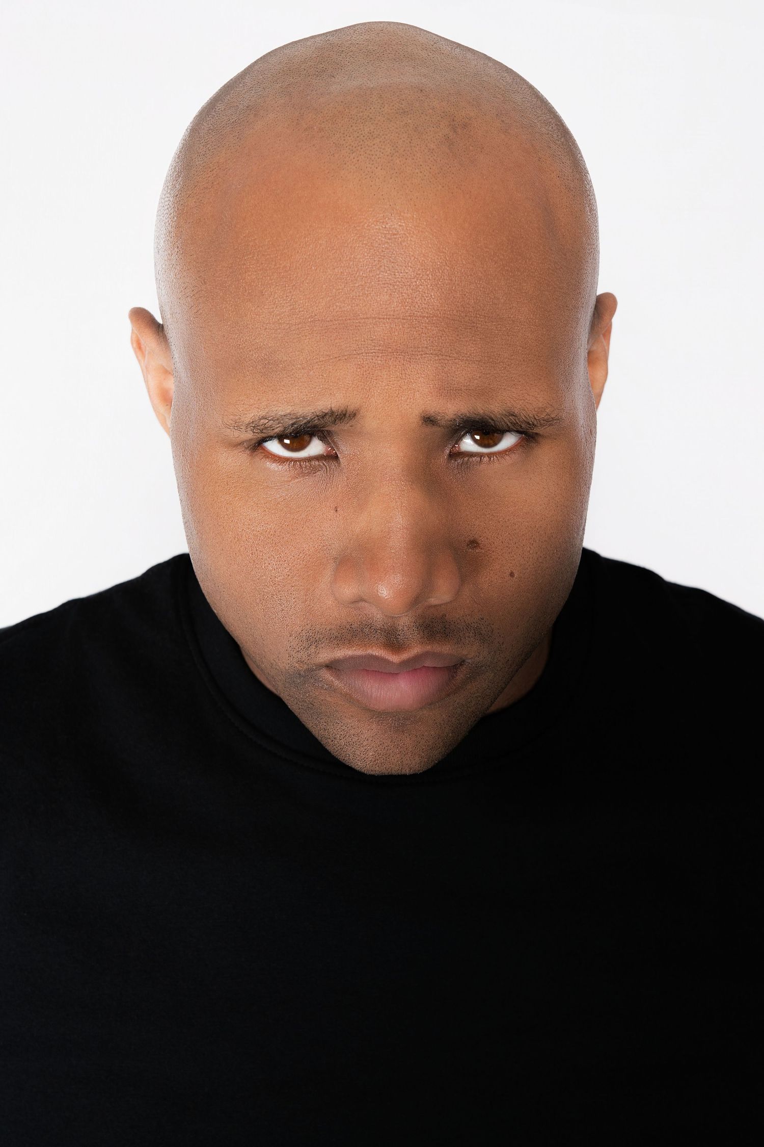 Bald man with furrowed brow in black t-shirt against white background.