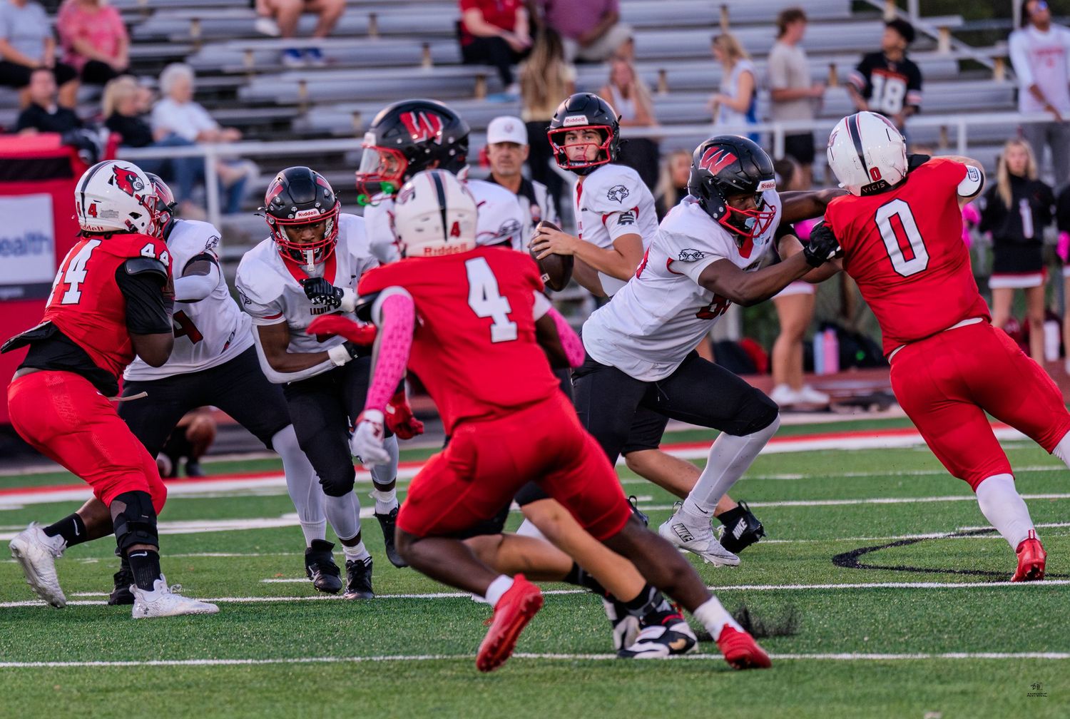 A quarterback scrambles through defenders during an action-packed high school football game at night.