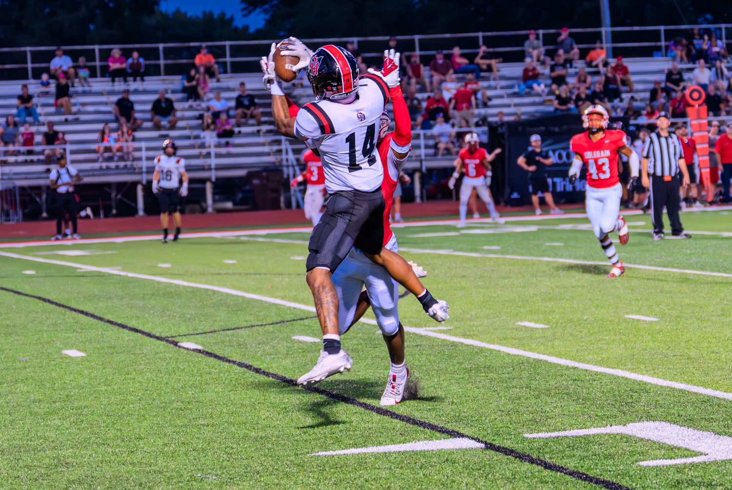 Player #14 makes a catch during a high school football game under stadium lights.