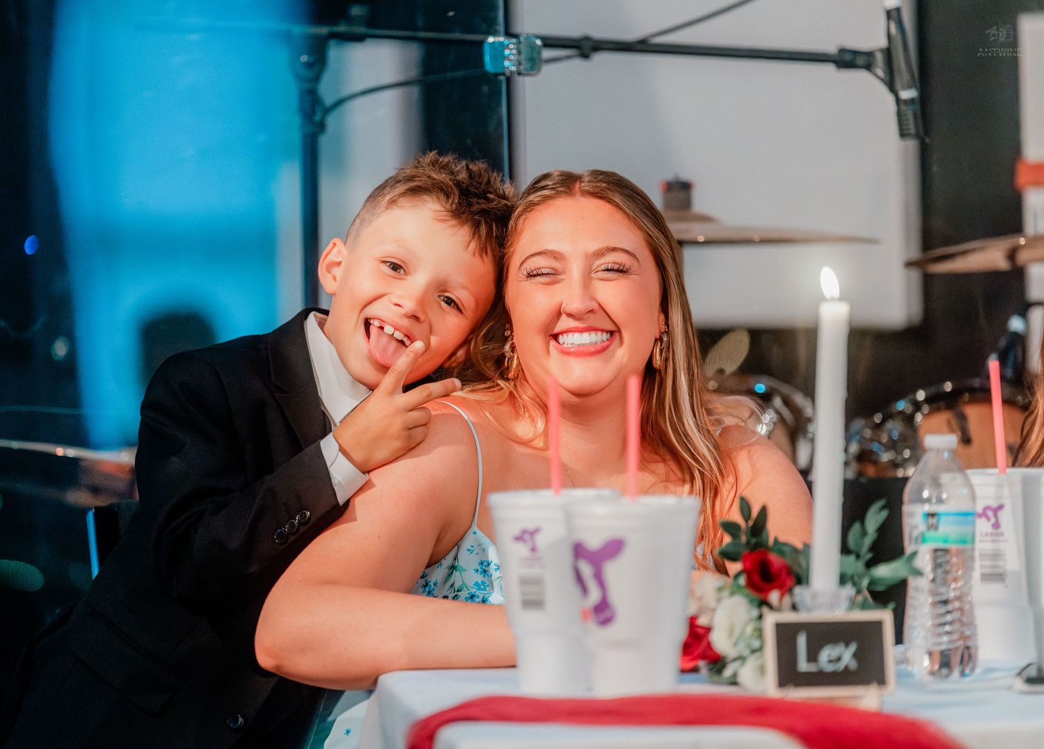 A young boy in a suit and a woman in a blue dress smile together at a wedding reception table.