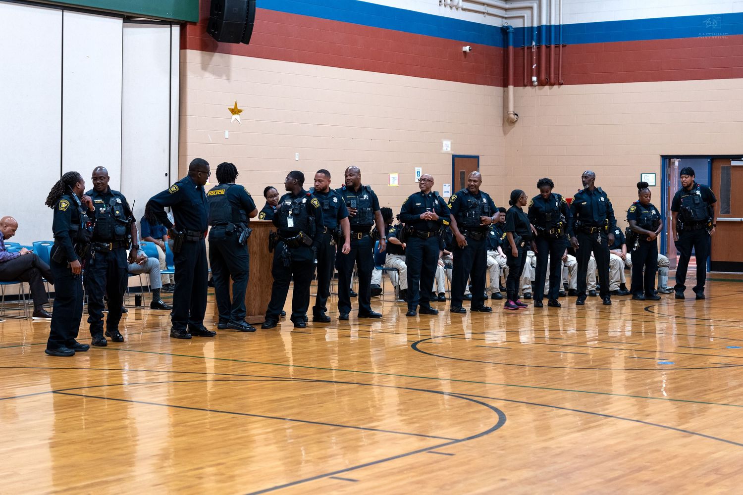 A group of police officers in uniform standing in a line inside a school gymnasium during an official ceremony.