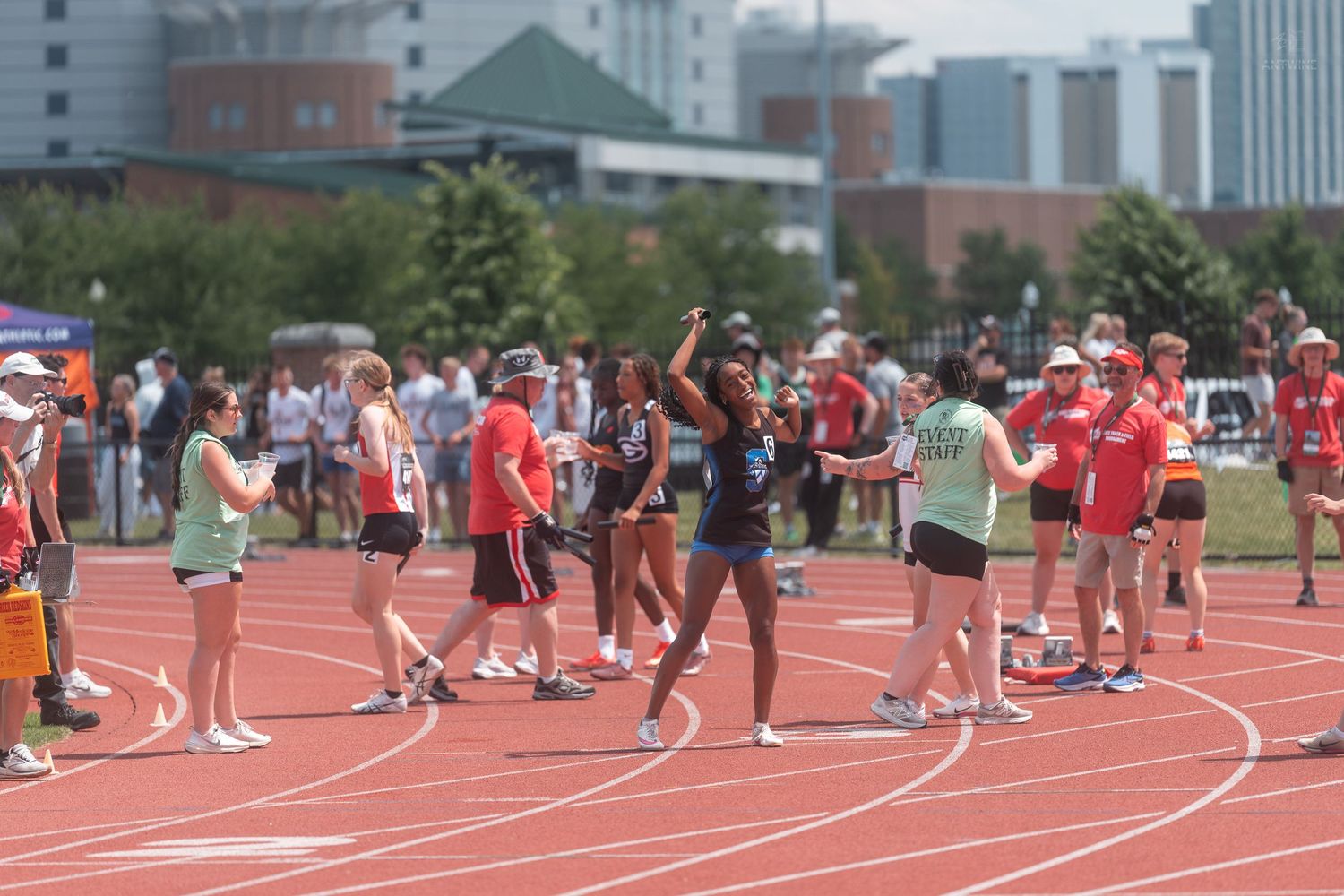 Female track and field athletes celebrate and interact on the red track at an OHSAA championship meet.