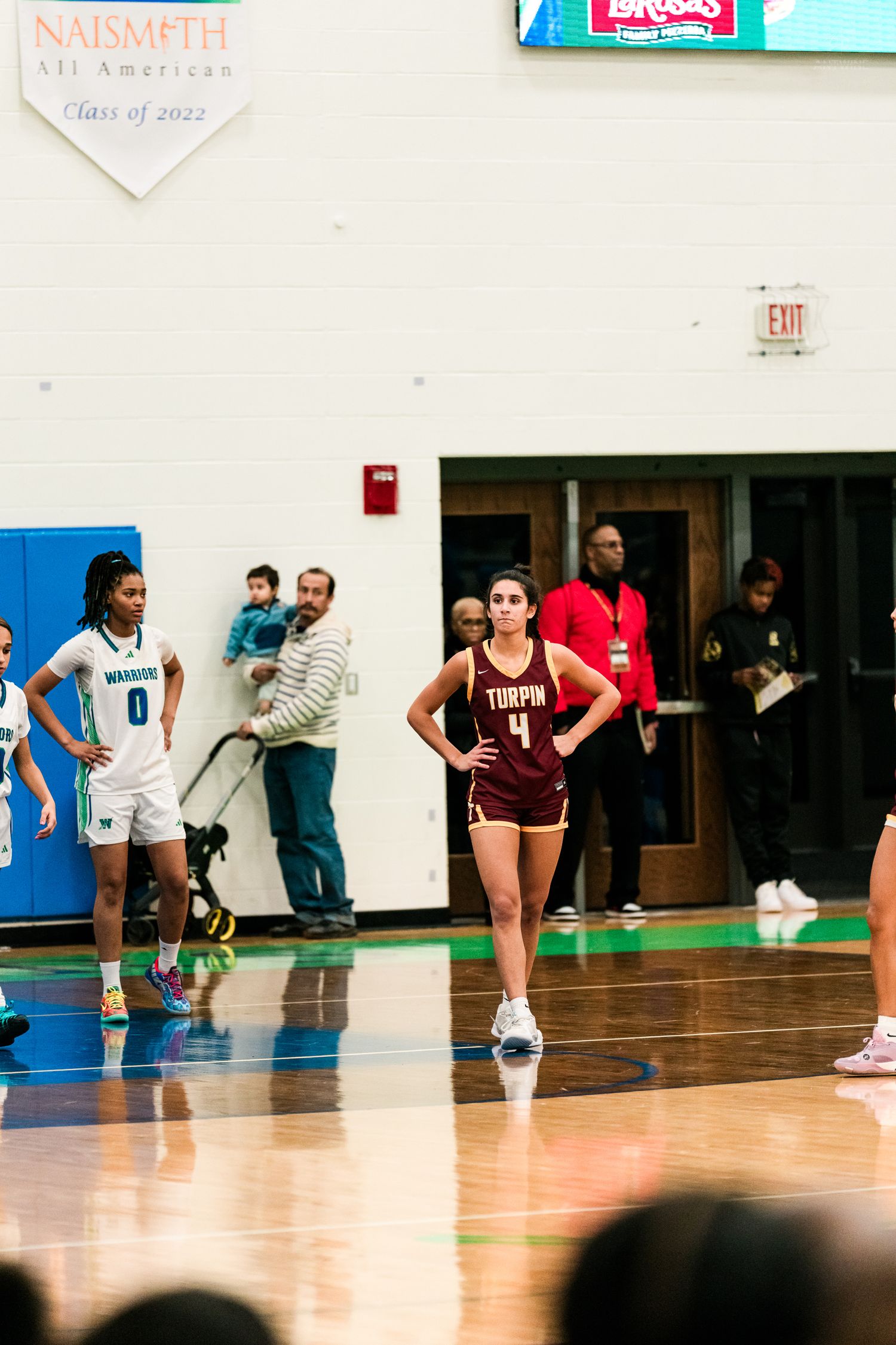 Turpin high school girls basketball player number 4 stands with hands on hips during a game in a blue gymnasium.