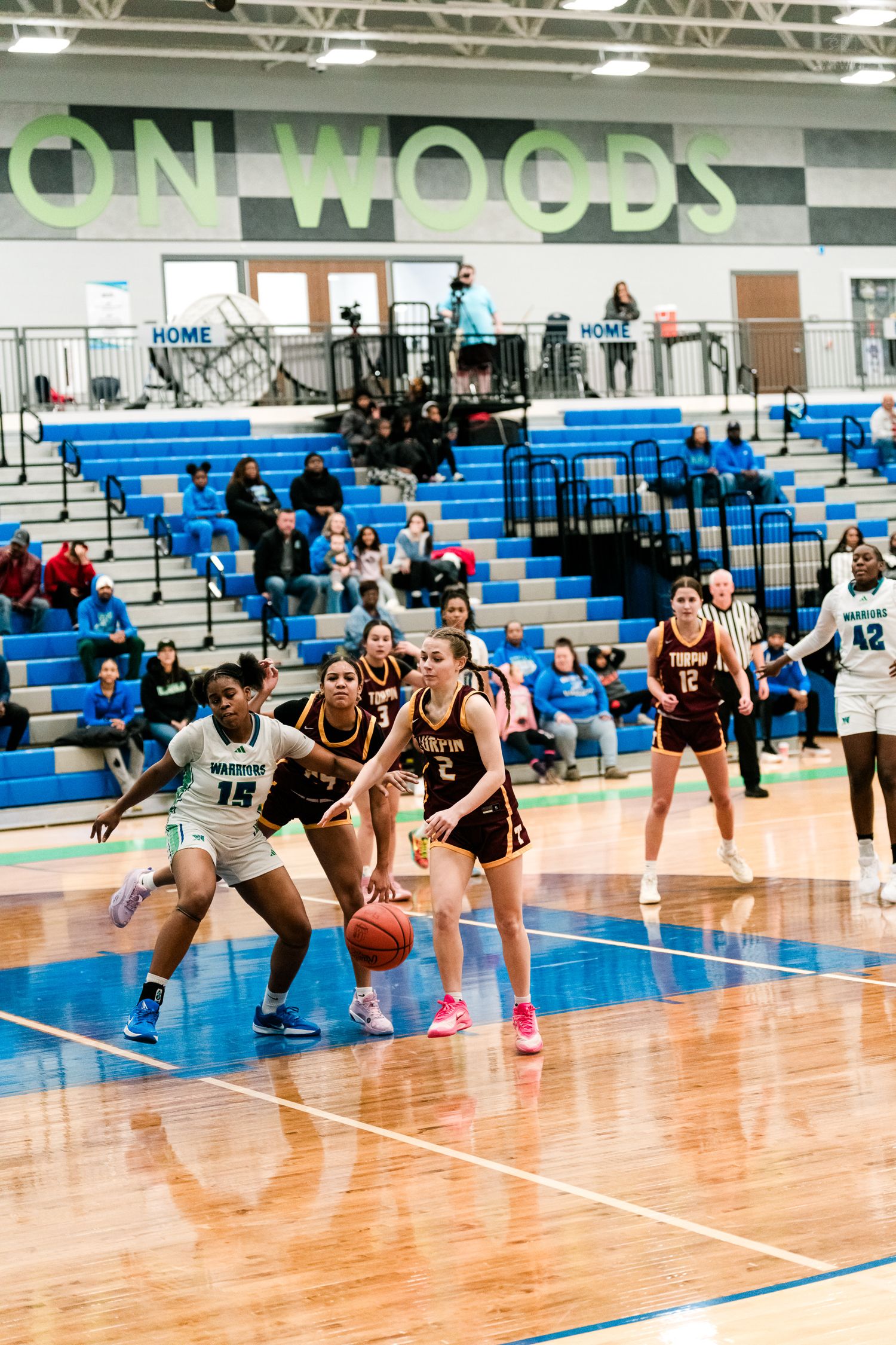 Girls basketball players compete on the court at Mason Woods gym as Turpin player #2 dribbles against Warriors defenders.